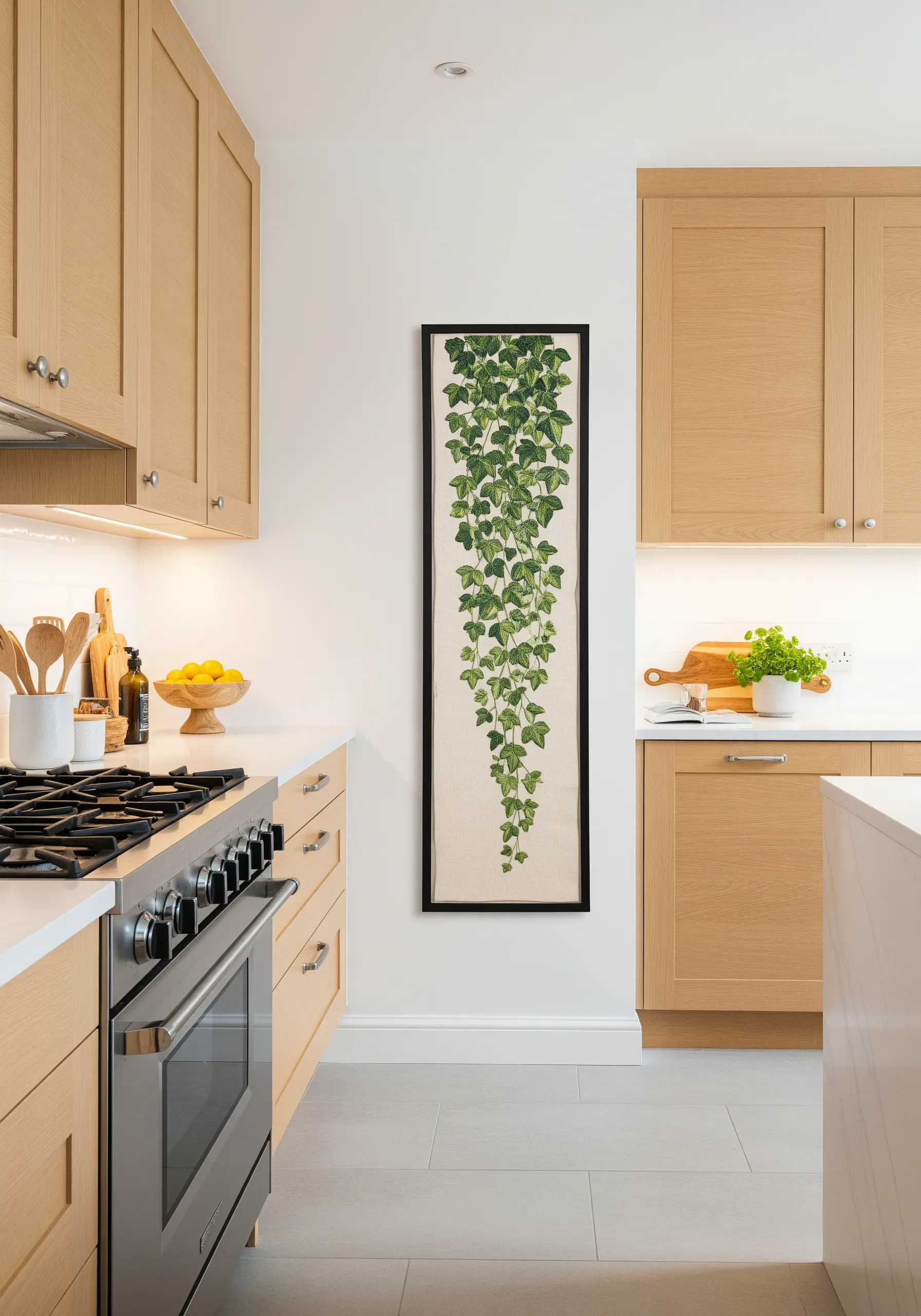 A tall, narrow framed embroidery of trailing ivy hanging in a modern kitchen