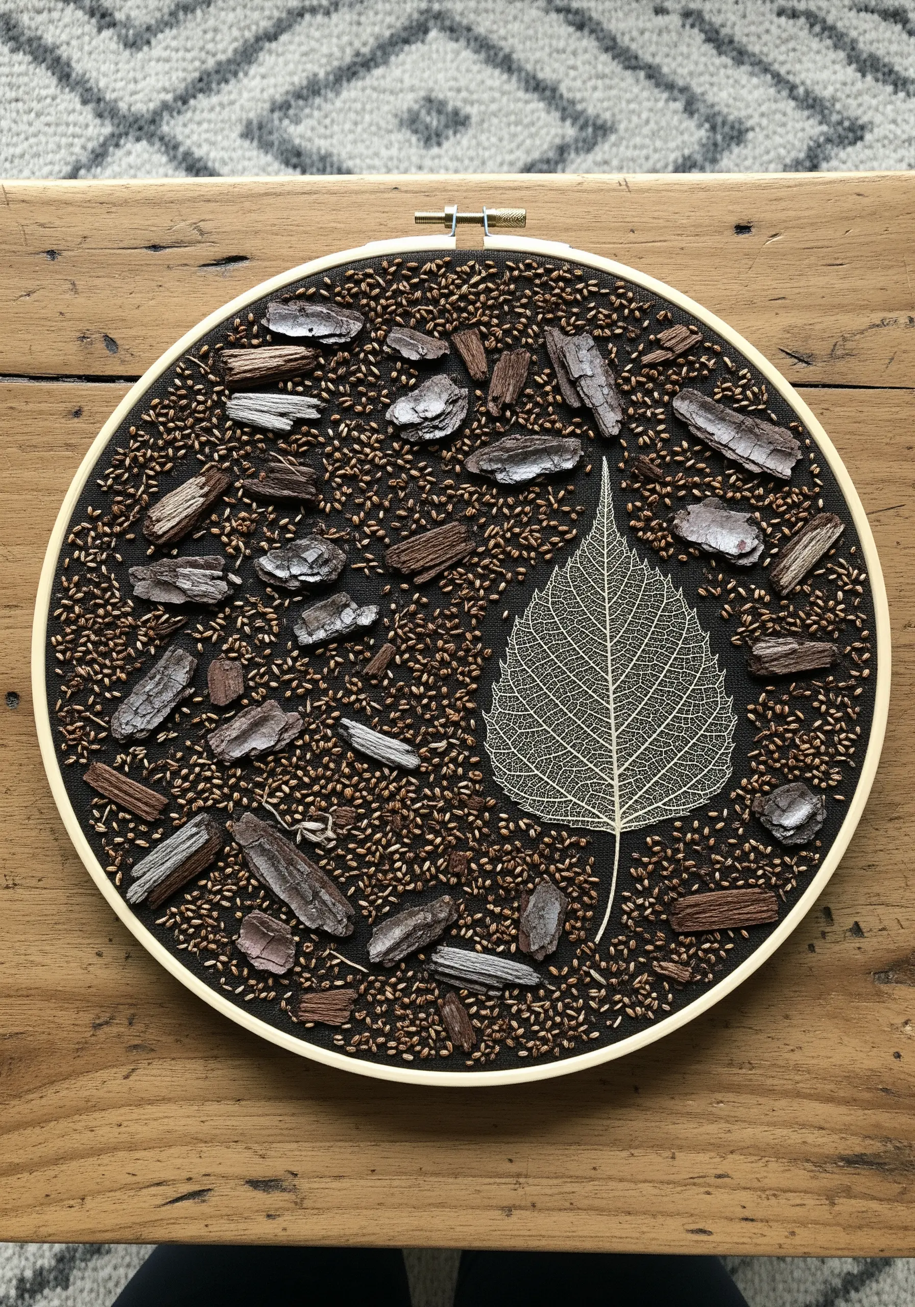 Mixed-media hoop art featuring real bark chips and a skeleton leaf on a stitched background.