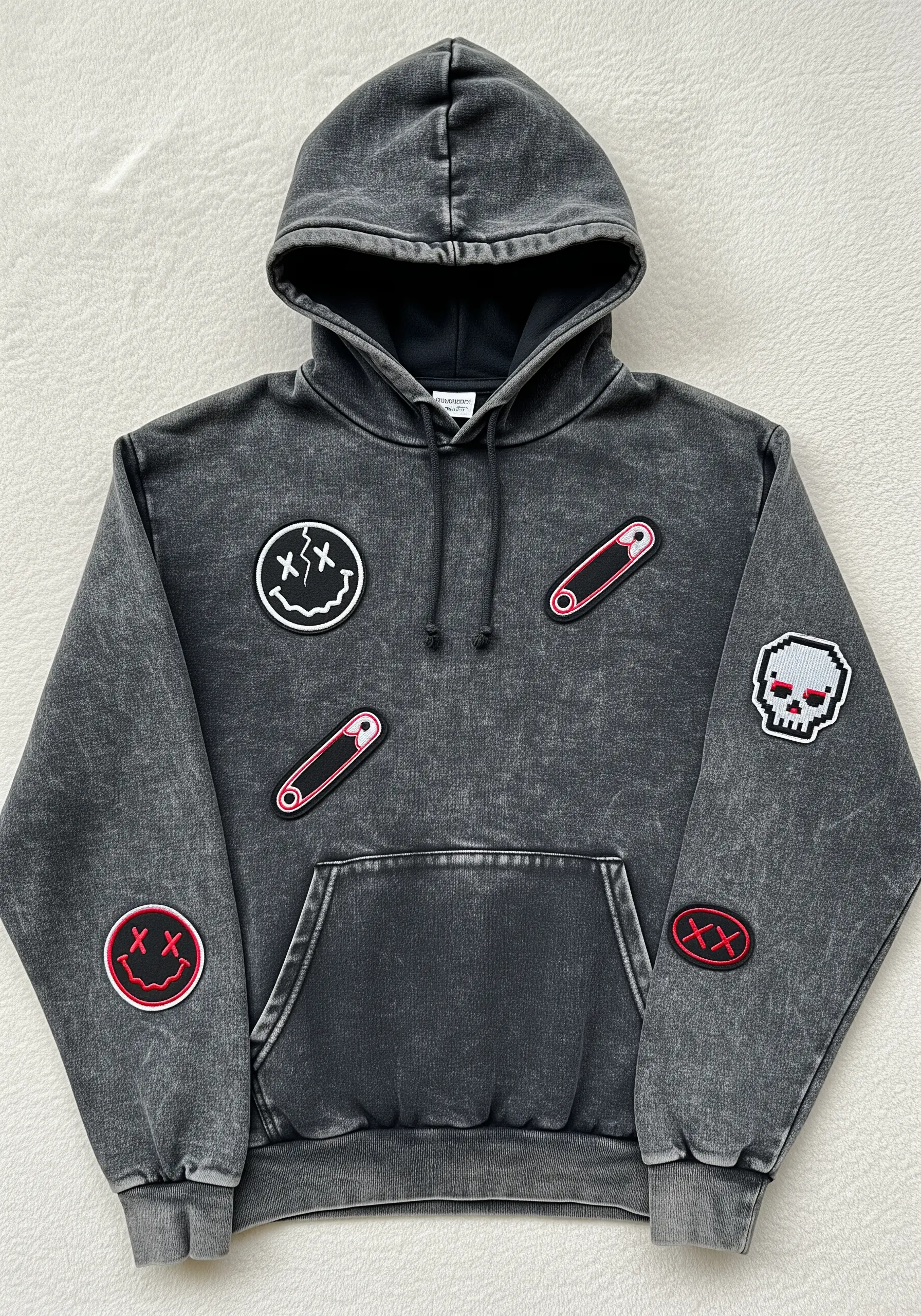 A washed-grey hoodie decorated with several embroidered patches, including smiley faces and safety pins.
