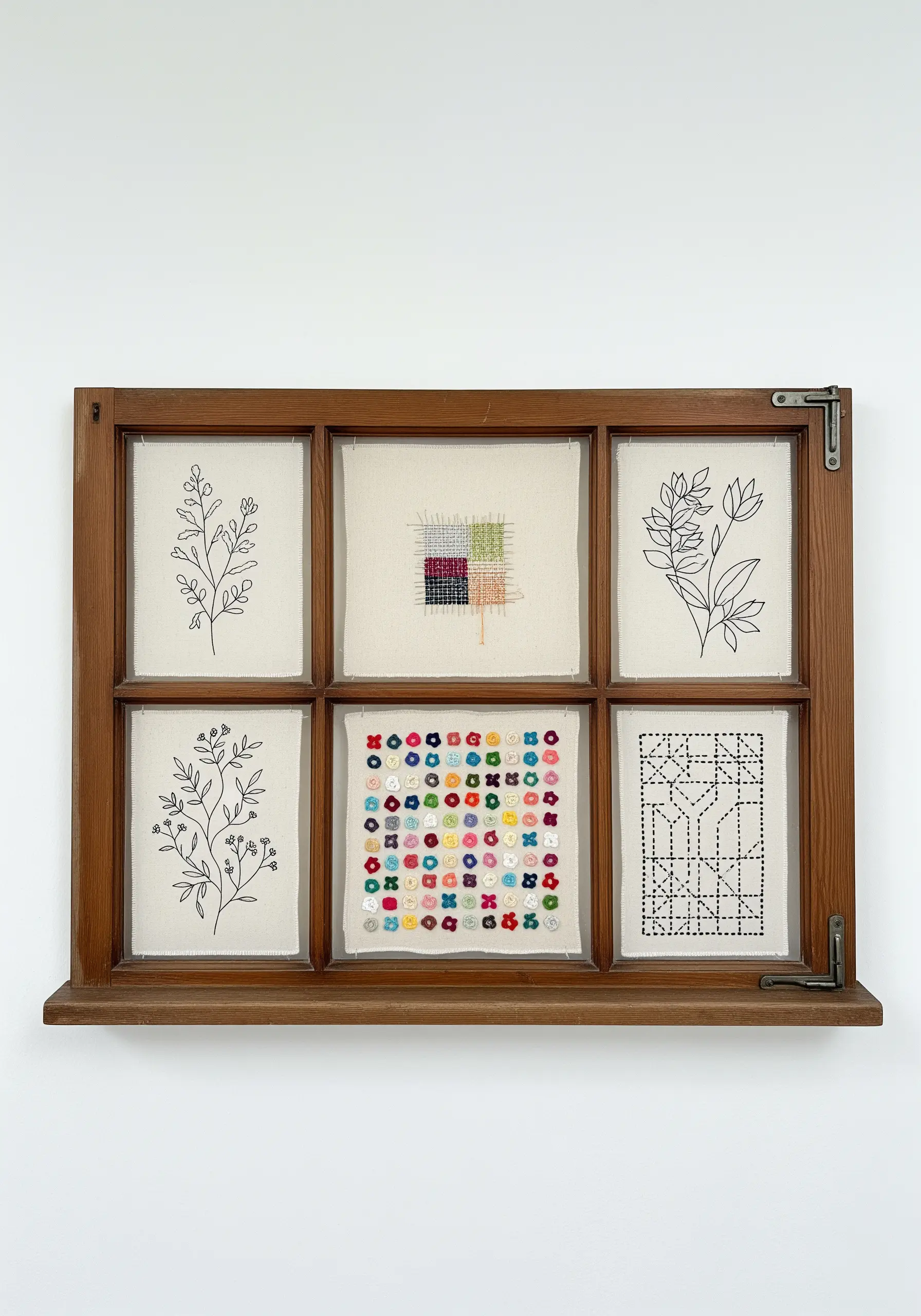 An old wooden window frame with six panes, each displaying a different small embroidery.
