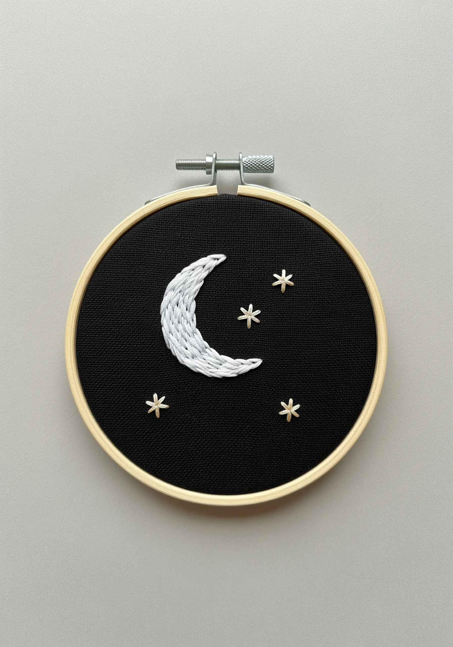 A crescent moon in white satin stitch with small gold stars on black fabric.