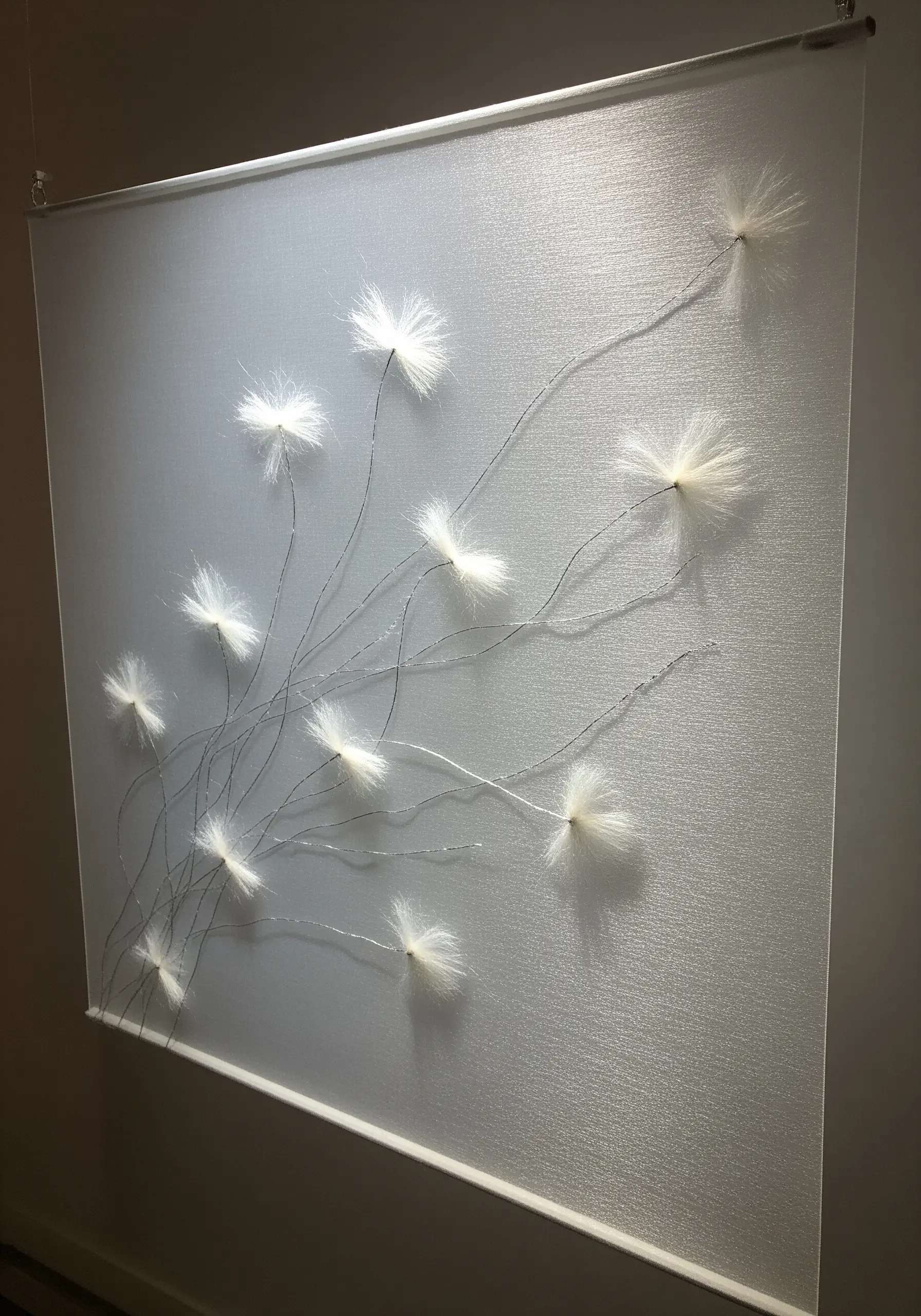 Embroidery of dandelion seeds floating across a sheer, translucent fabric panel.