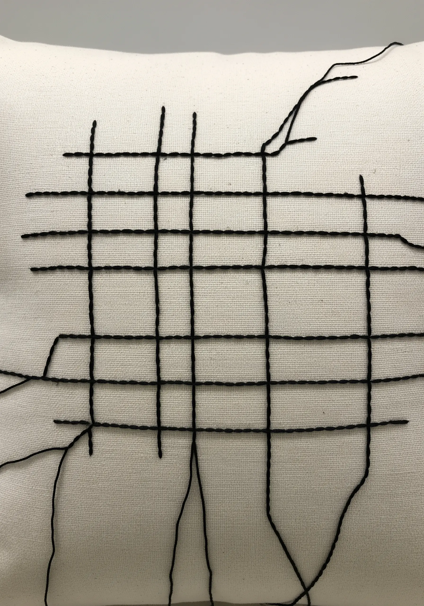 A black thread grid on a white pillow with intentionally loose, trailing threads.