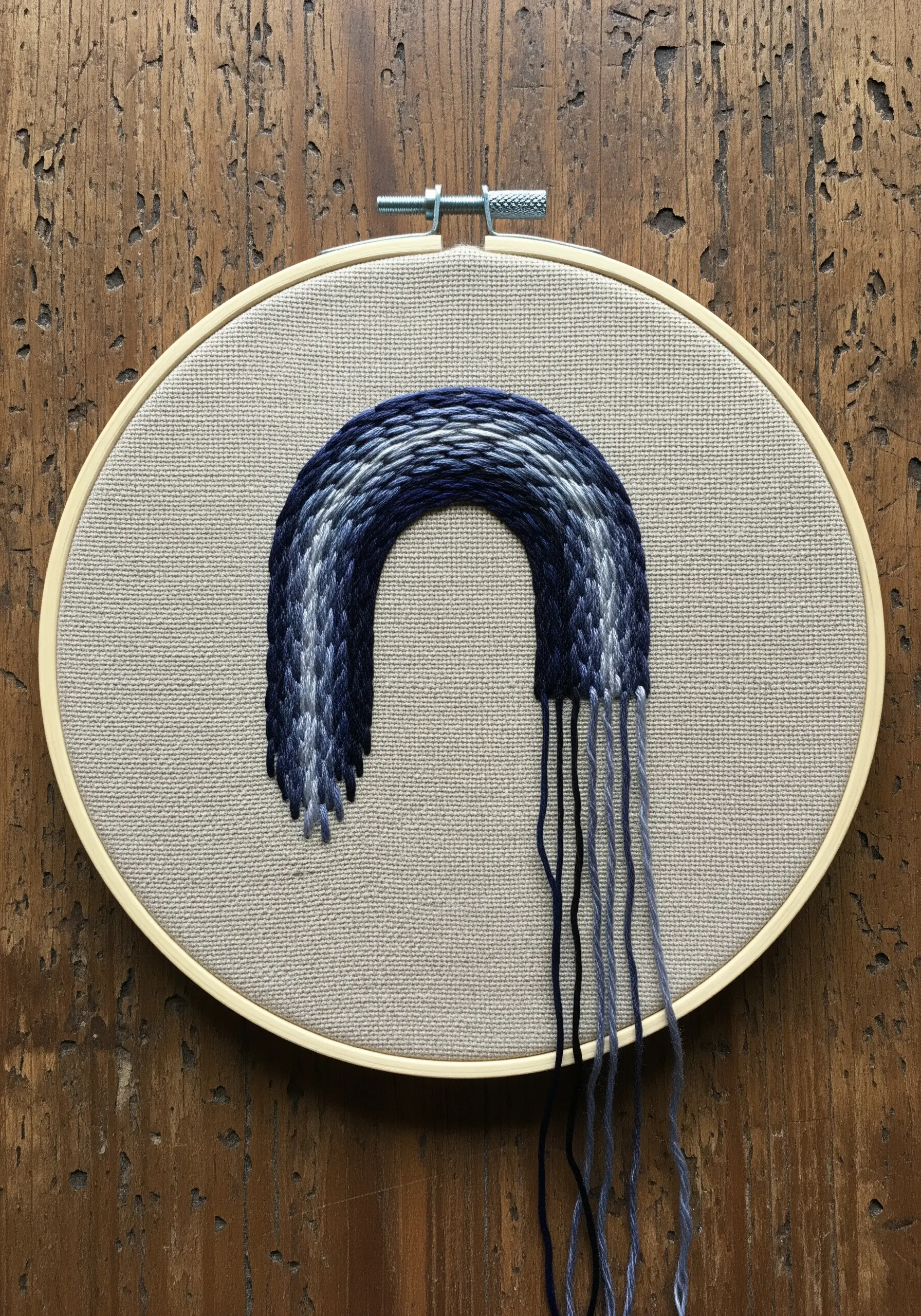 Abstract woven arch in shades of blue with threads left hanging loose.