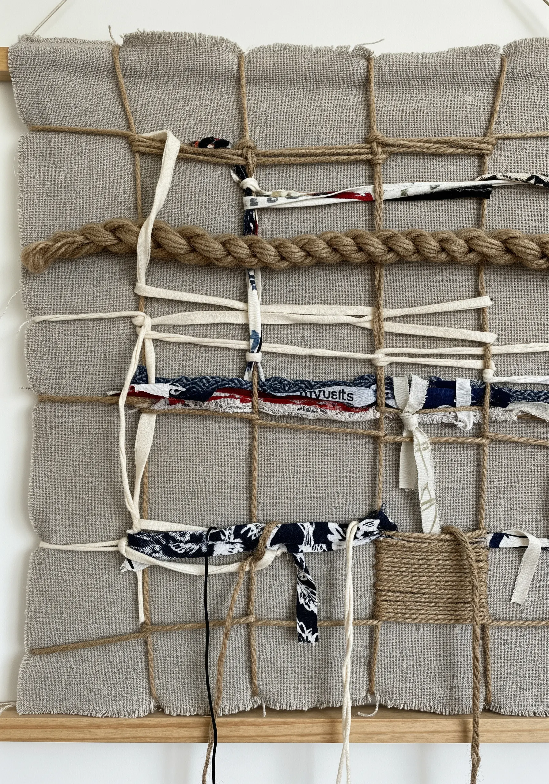 An open-weave wall hanging made with jute twine, thick rope, and torn fabric strips.