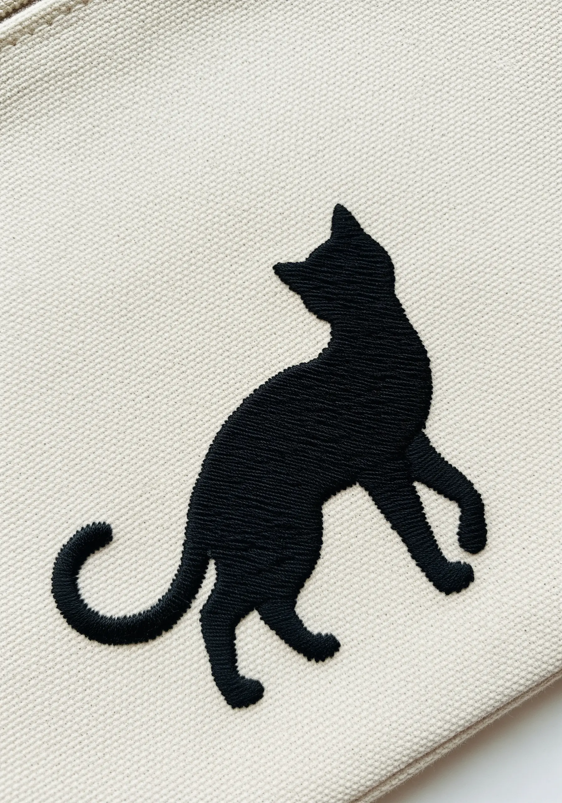 A solid black cat silhouette with a sharp outline embroidered on a canvas pouch.