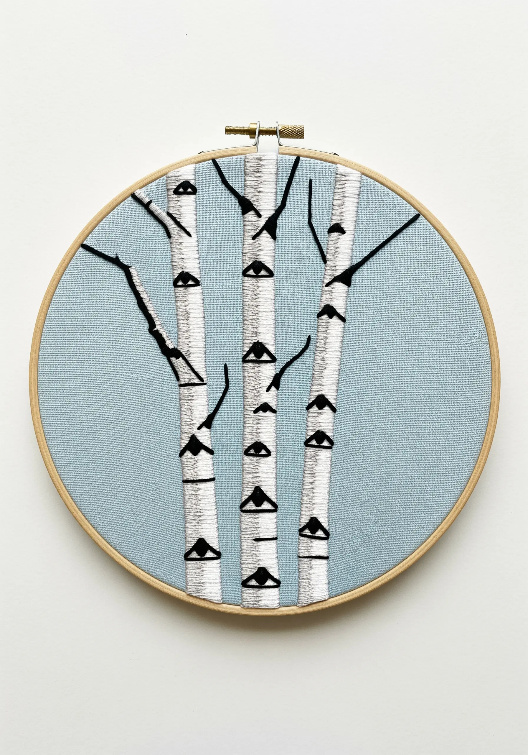 Minimalist embroidery of three birch trees with graphic black knots on blue fabric.
