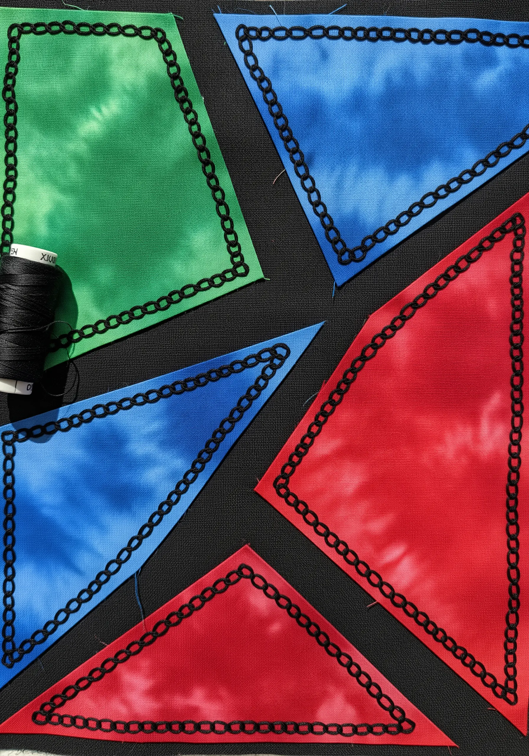 Geometric shapes in tie-dyed red, green, and blue fabric outlined with black chain stitch on a black base.