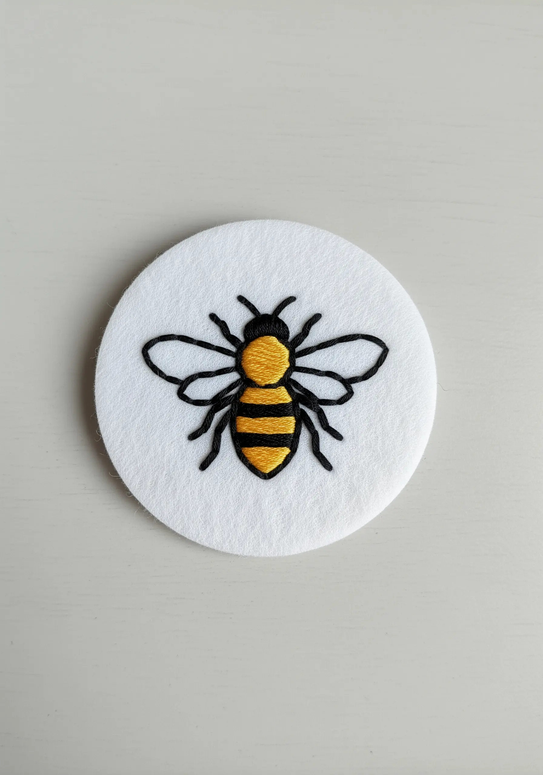 A honeybee with yellow and black stripes, embroidered with sharp black outlines on white felt.