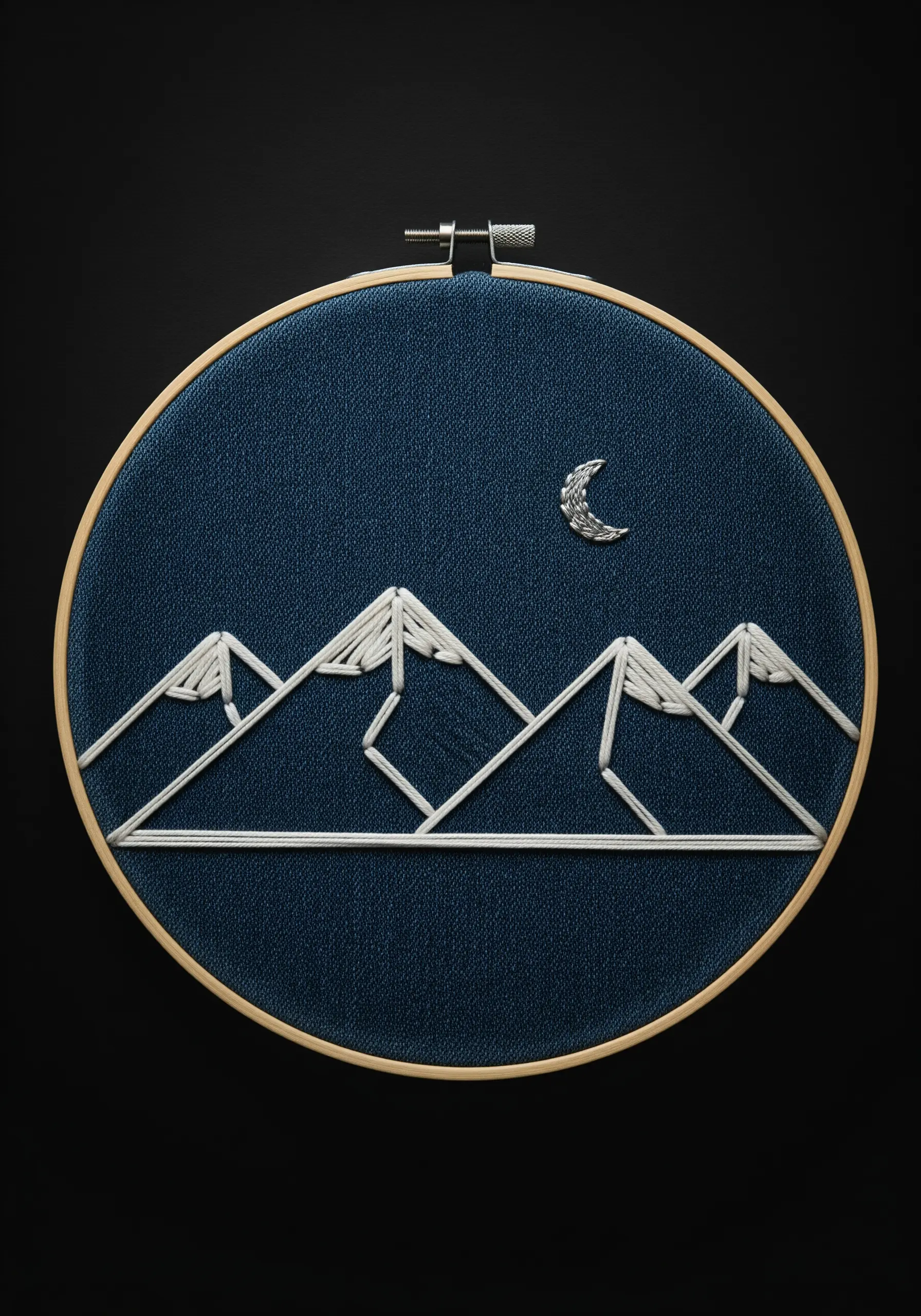 Minimalist embroidery of geometric mountain outlines and a textured silver moon on dark blue fabric.