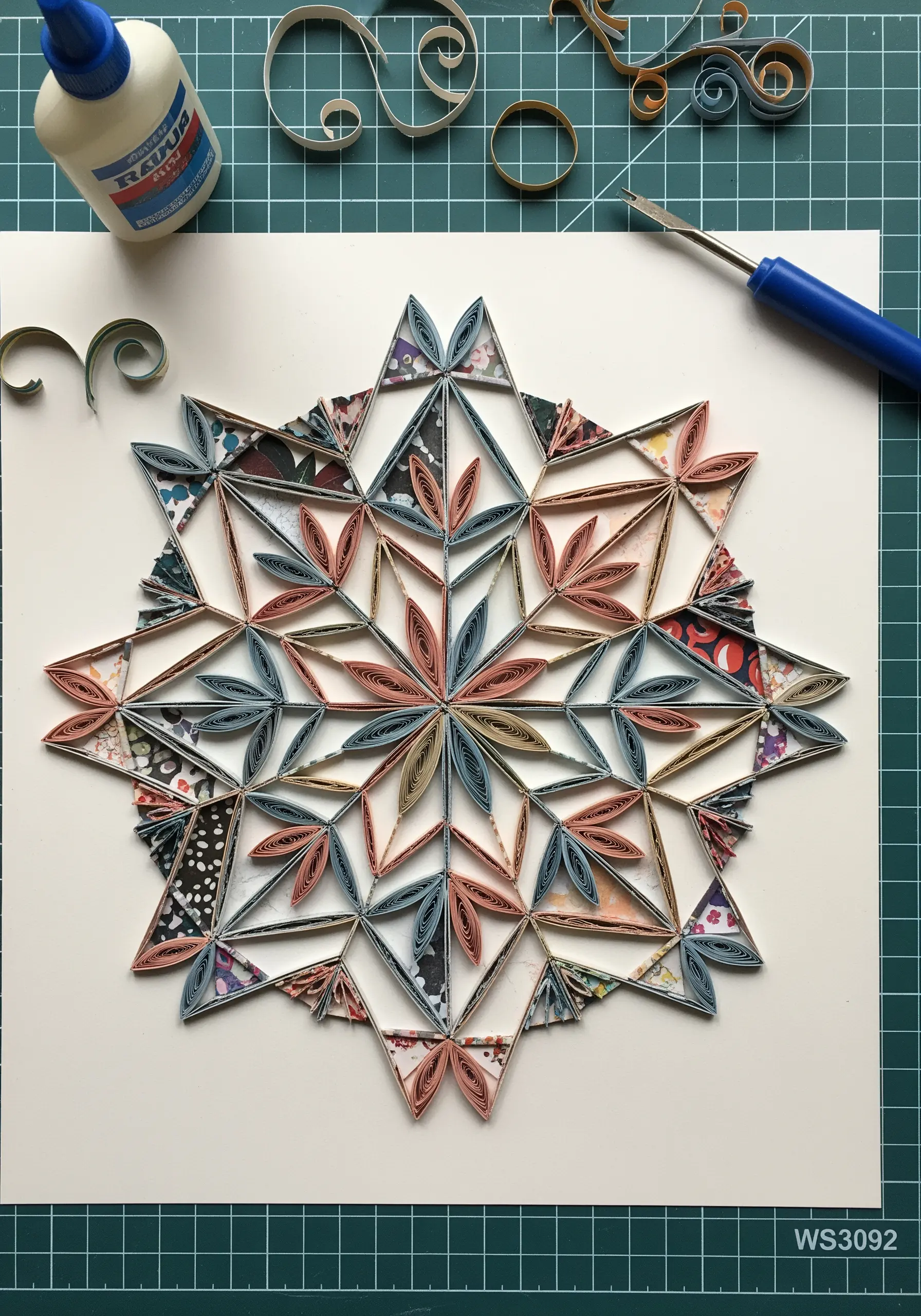 A complex geometric mandala made from curled strips of patterned paper.