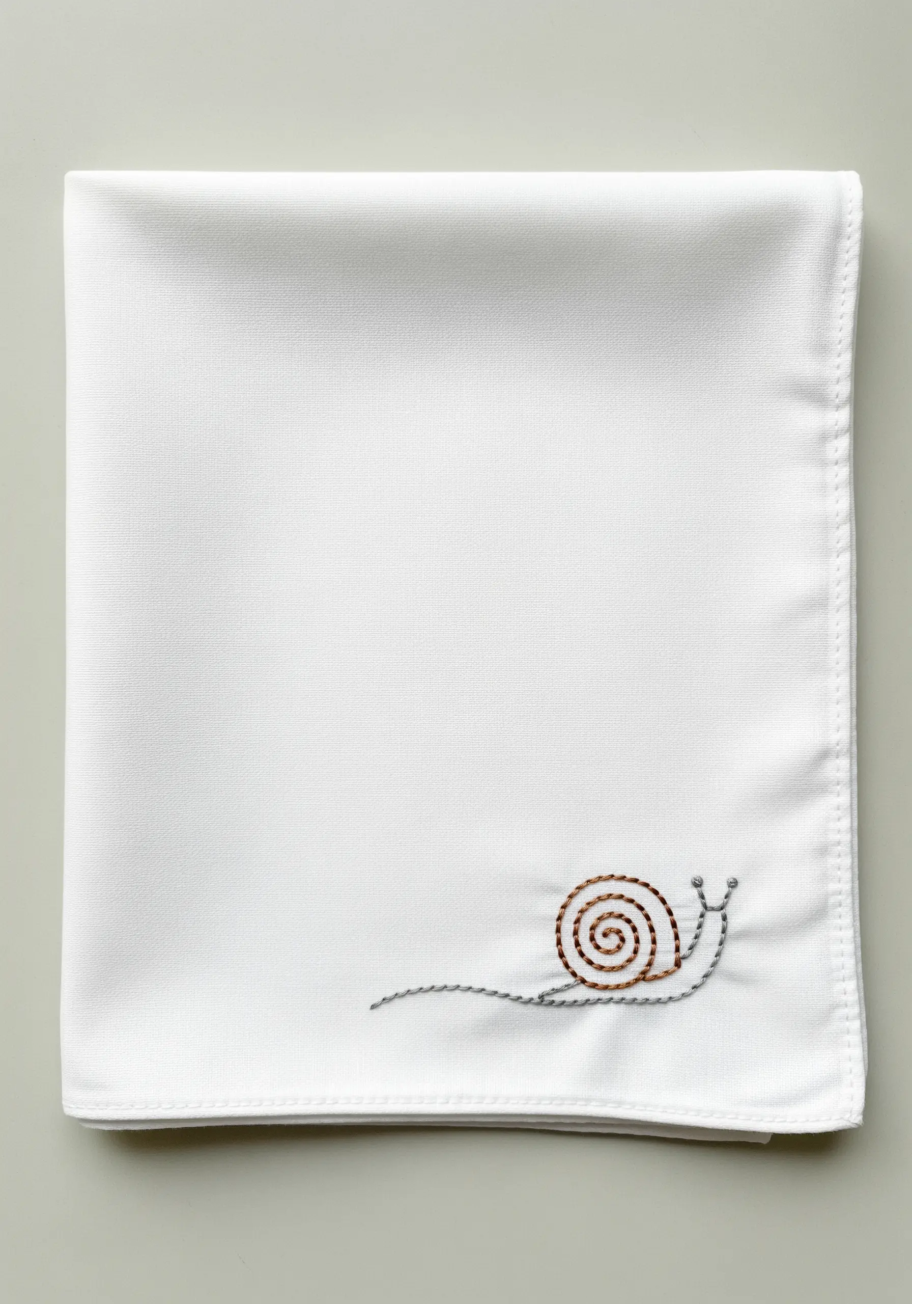 A small snail embroidered on the corner of a white handkerchief.