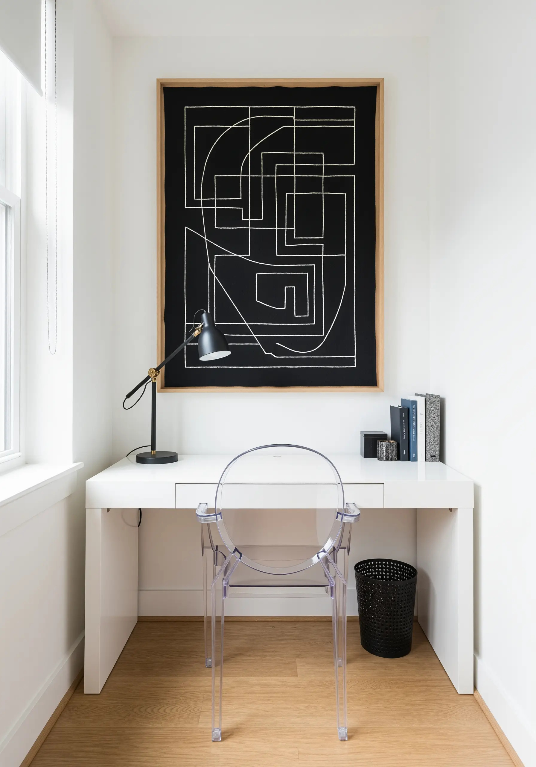 Large framed black canvas with abstract, geometric white line embroidery over a modern desk.