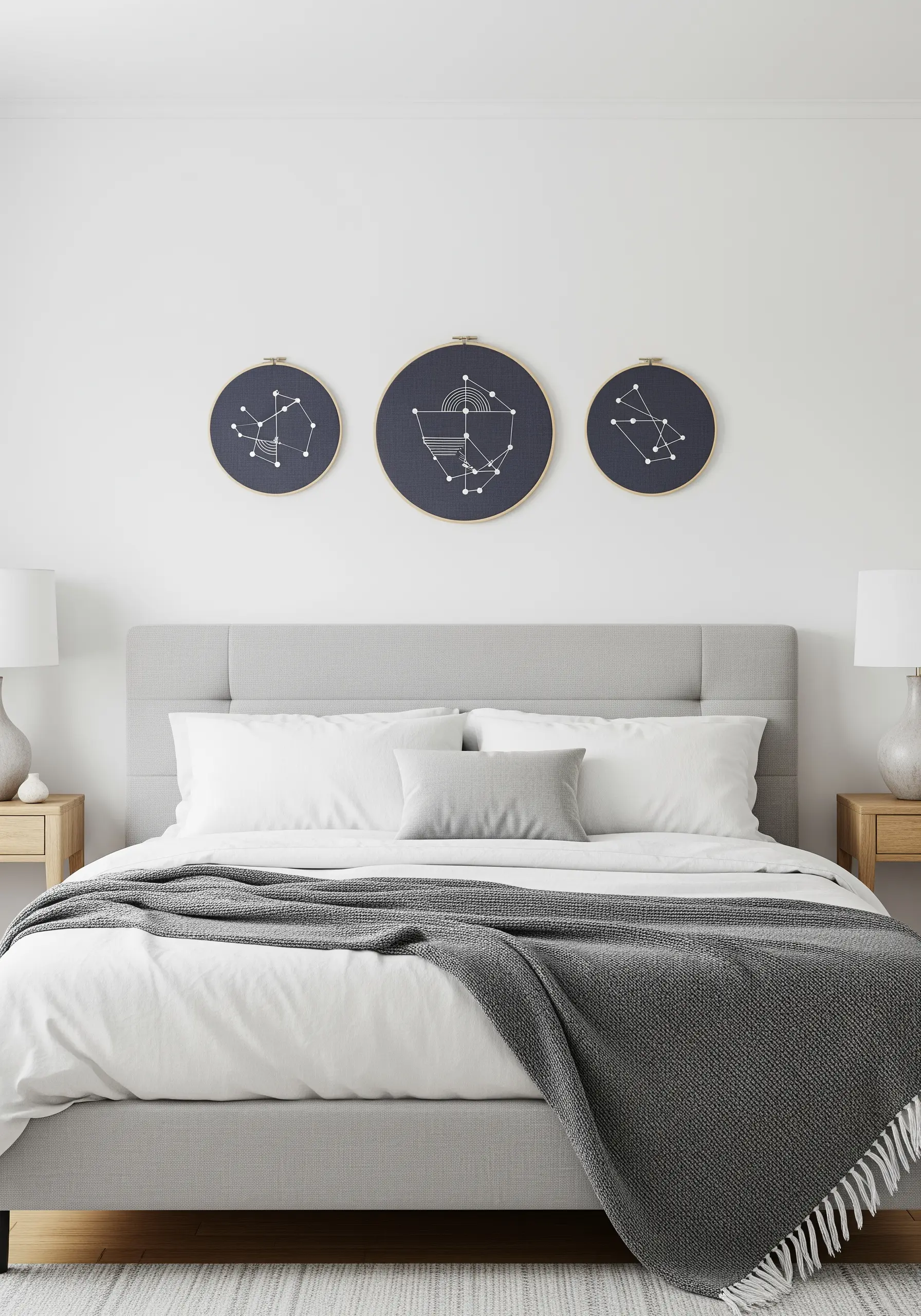 Three embroidery hoops with minimalist constellation patterns on dark blue fabric over a bed.