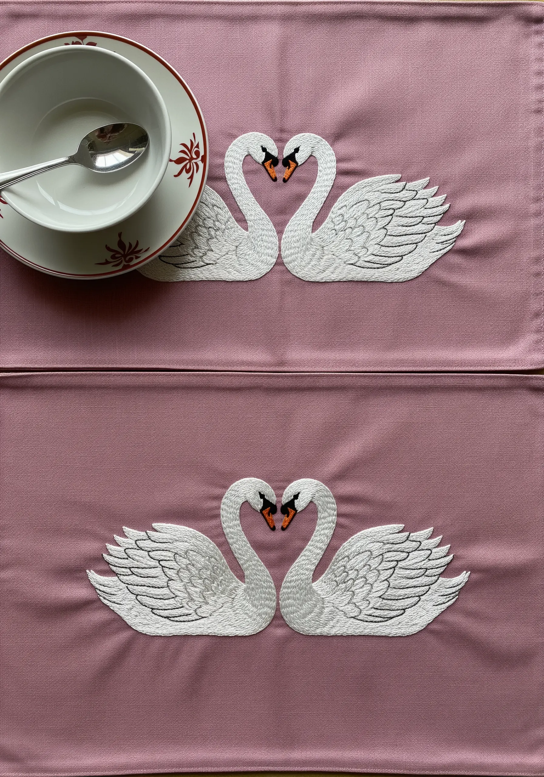 Two white swans facing each other to form a heart on a pink placemat.