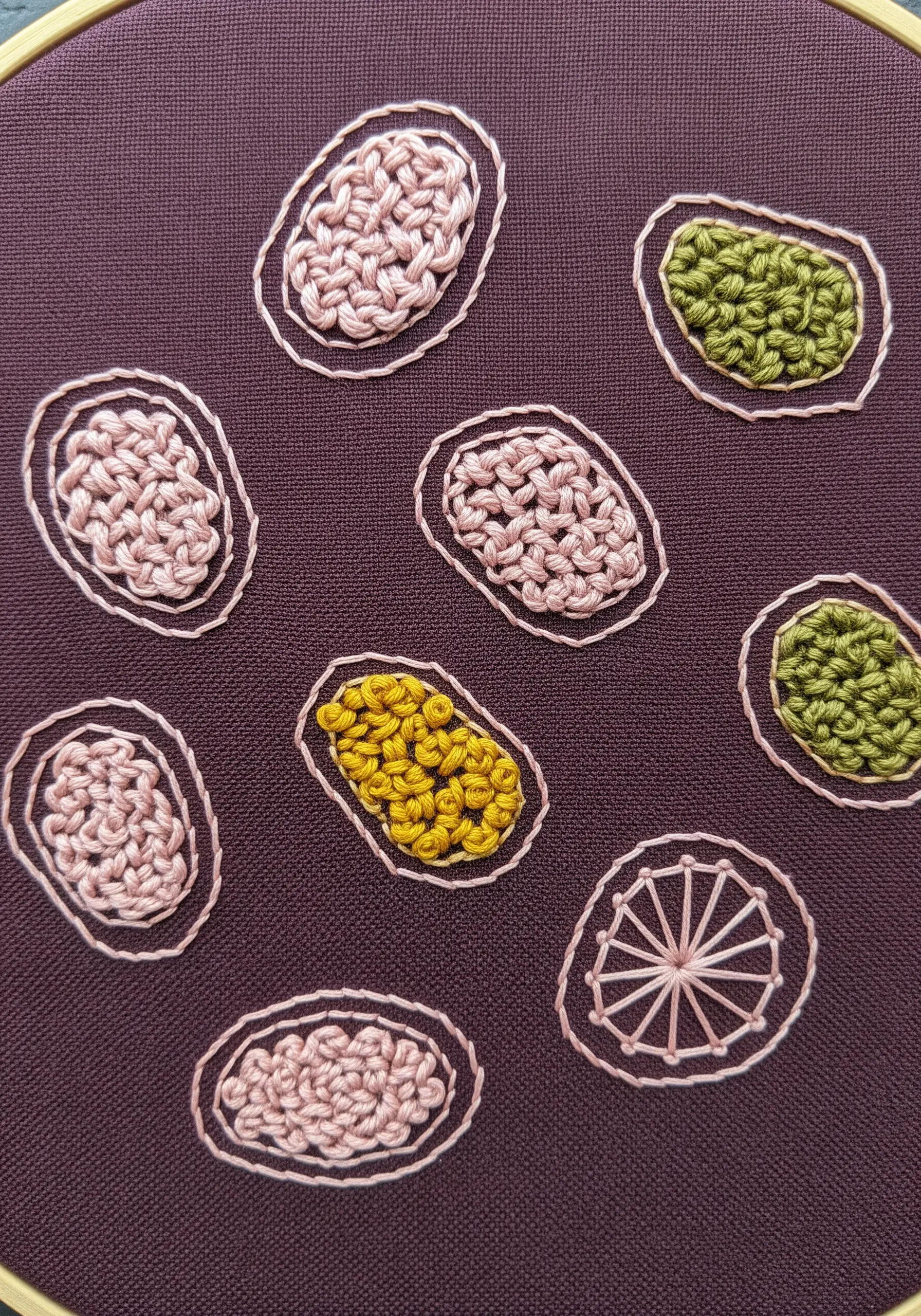 Small woven ovals in pink, green, and yellow, each defined by a light-colored backstitch outline.