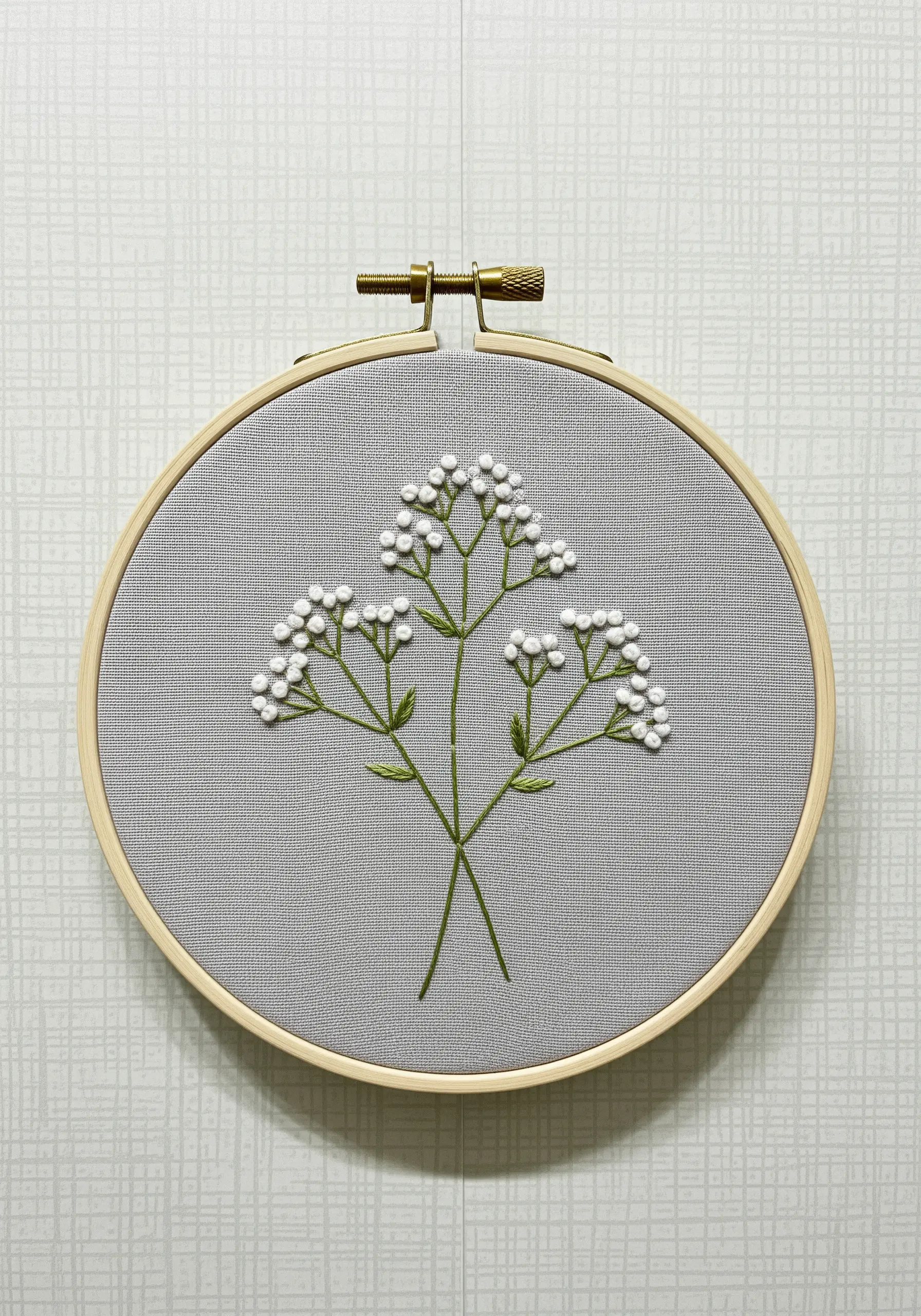 A spray of baby's breath made with tiny white French knots on grey fabric.