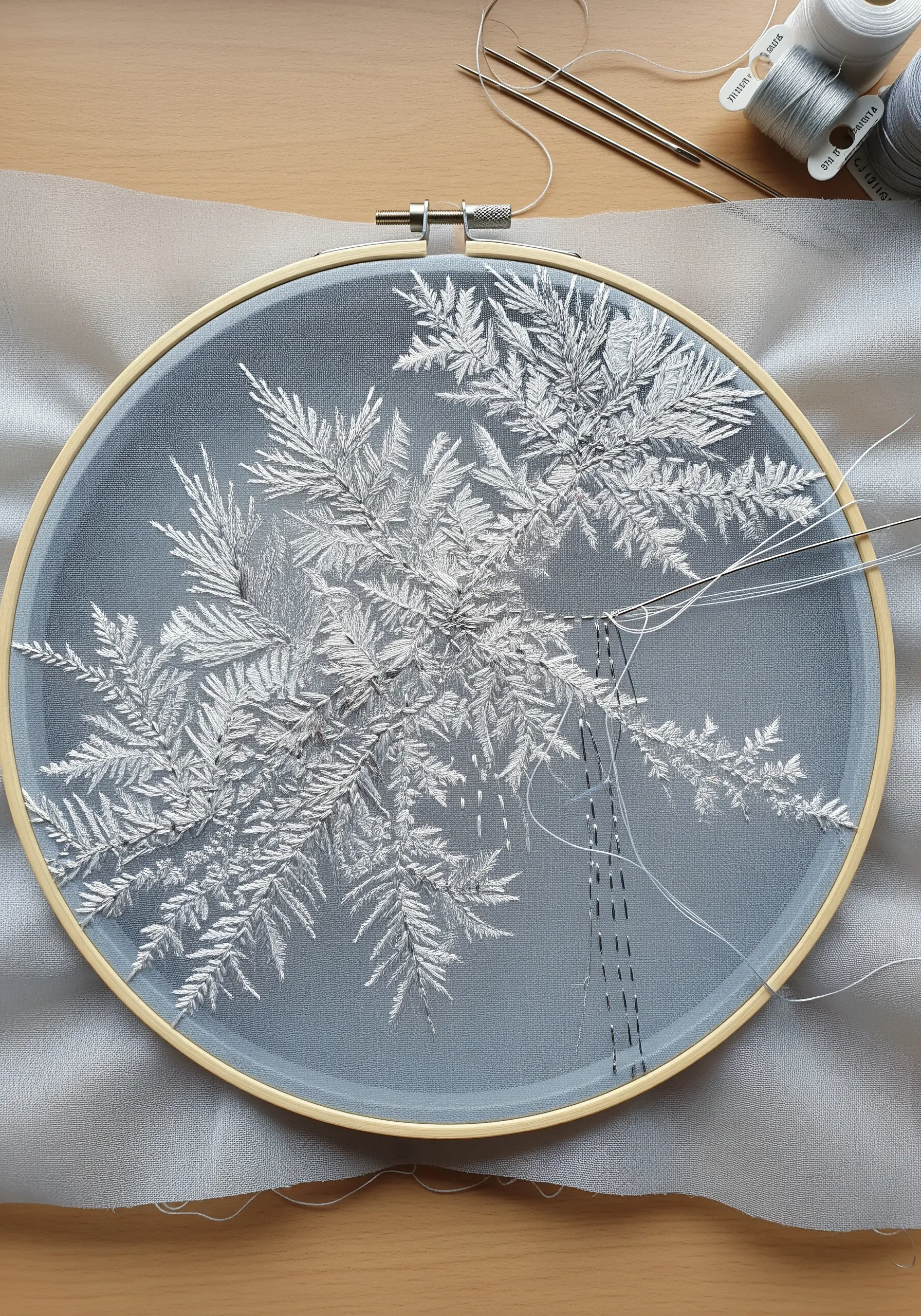 Delicate white embroidery of frost patterns on a sheer gray fabric inside a hoop.