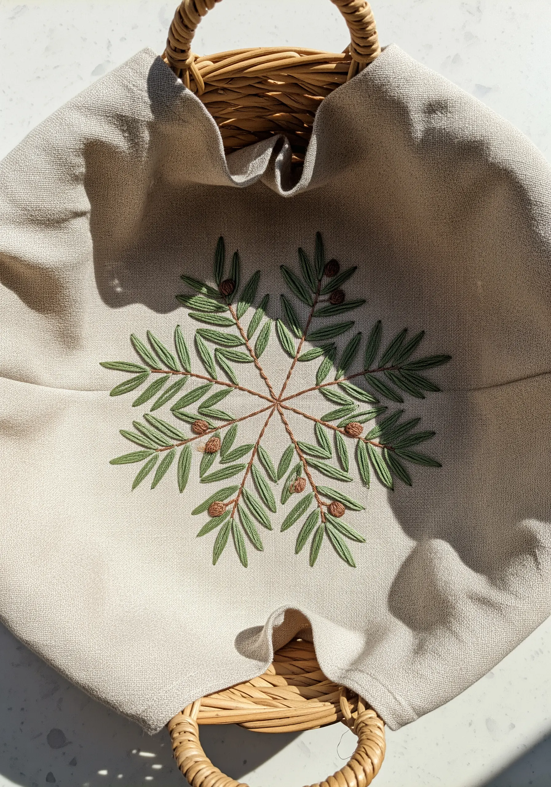 An embroidered olive branch mandala with French knot details on a linen basket liner.