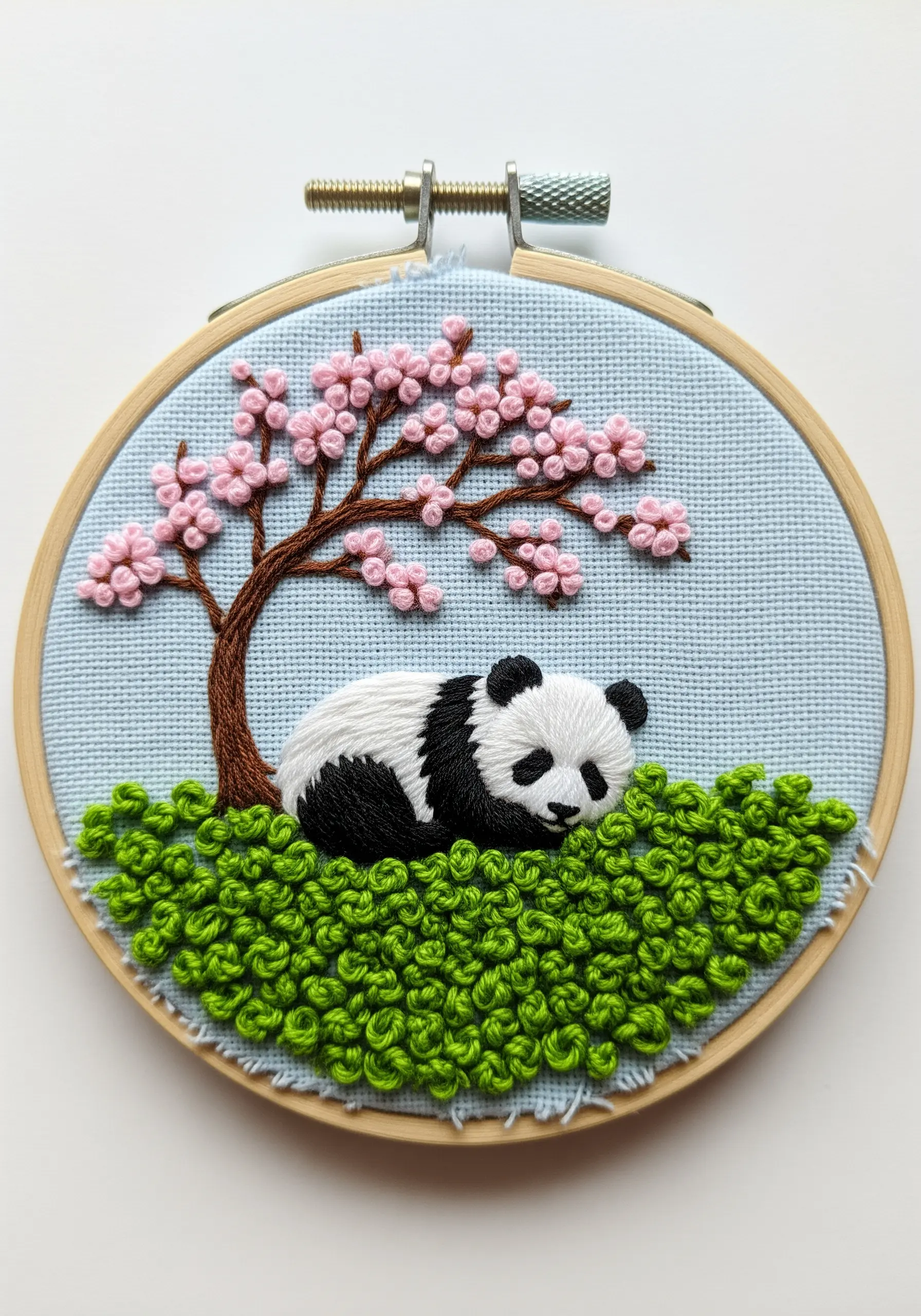 A sleeping panda in a hoop, nestled on a vibrant green hill made entirely of French knots.