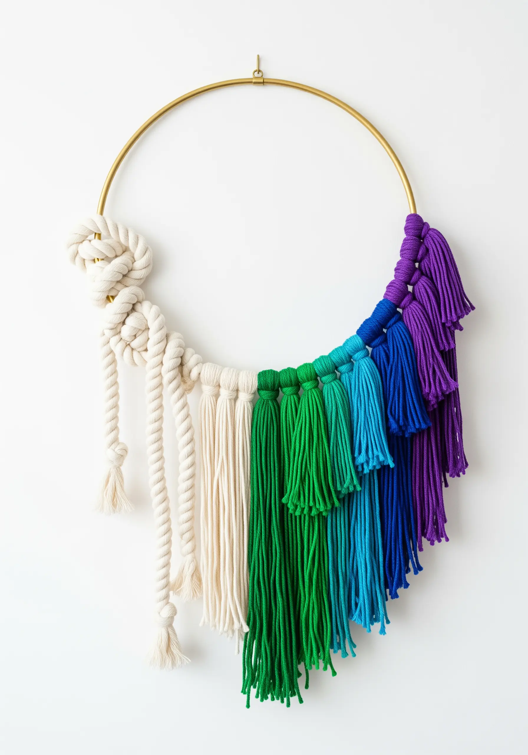 A brass hoop decorated with a chunky white knot and a rainbow cascade of tassels.