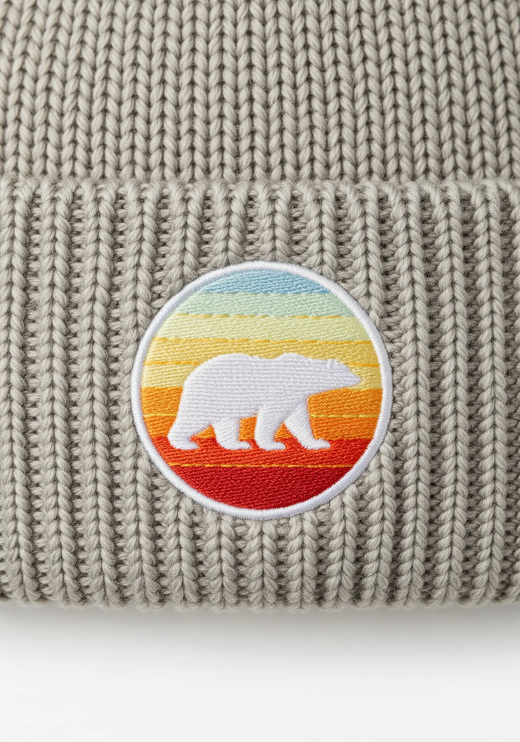 A clean, circular embroidered patch of a polar bear silhouette against a sunset on a ribbed beanie.