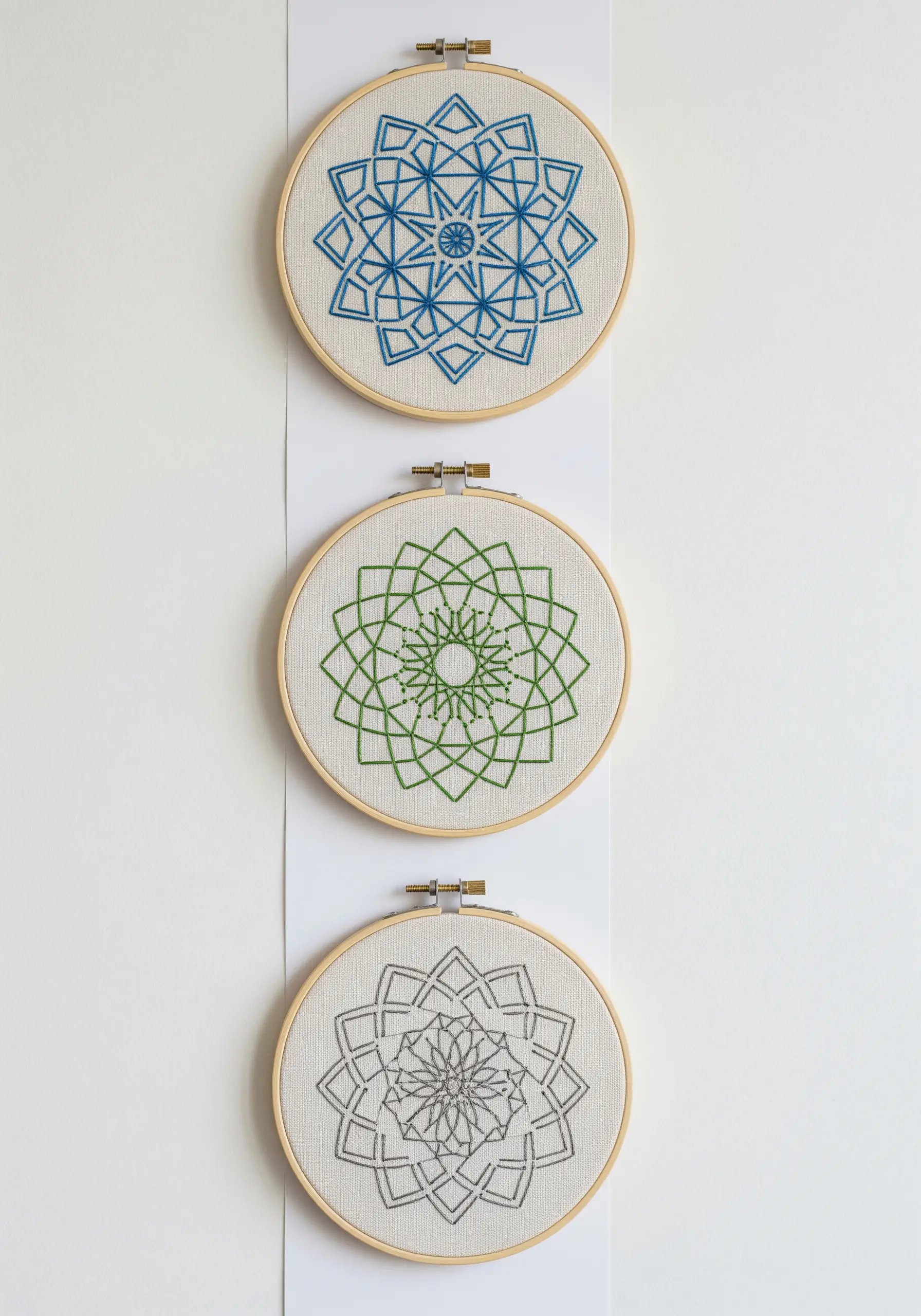 A series of three small mandalas with the same geometric pattern, stitched in blue, green, and gray.