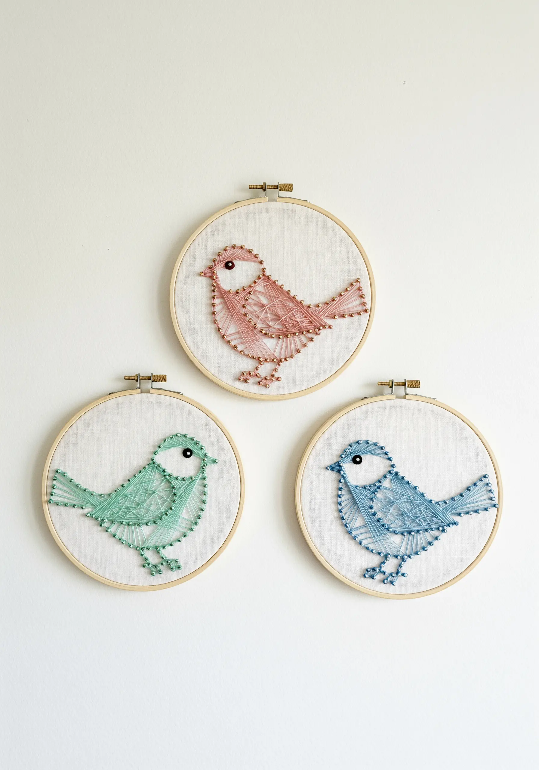 A set of three embroidery hoops, each with a bird stitched in a different pastel color.