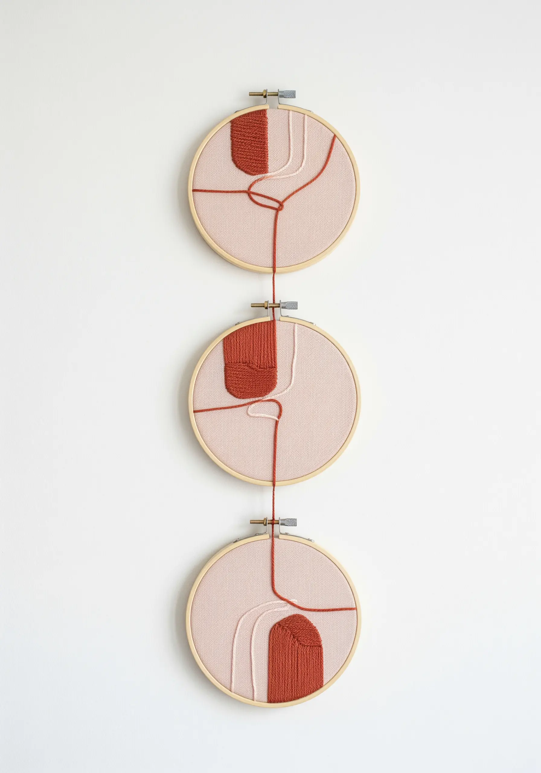 A vertical triptych of three embroidery hoops connected by a single red thread.