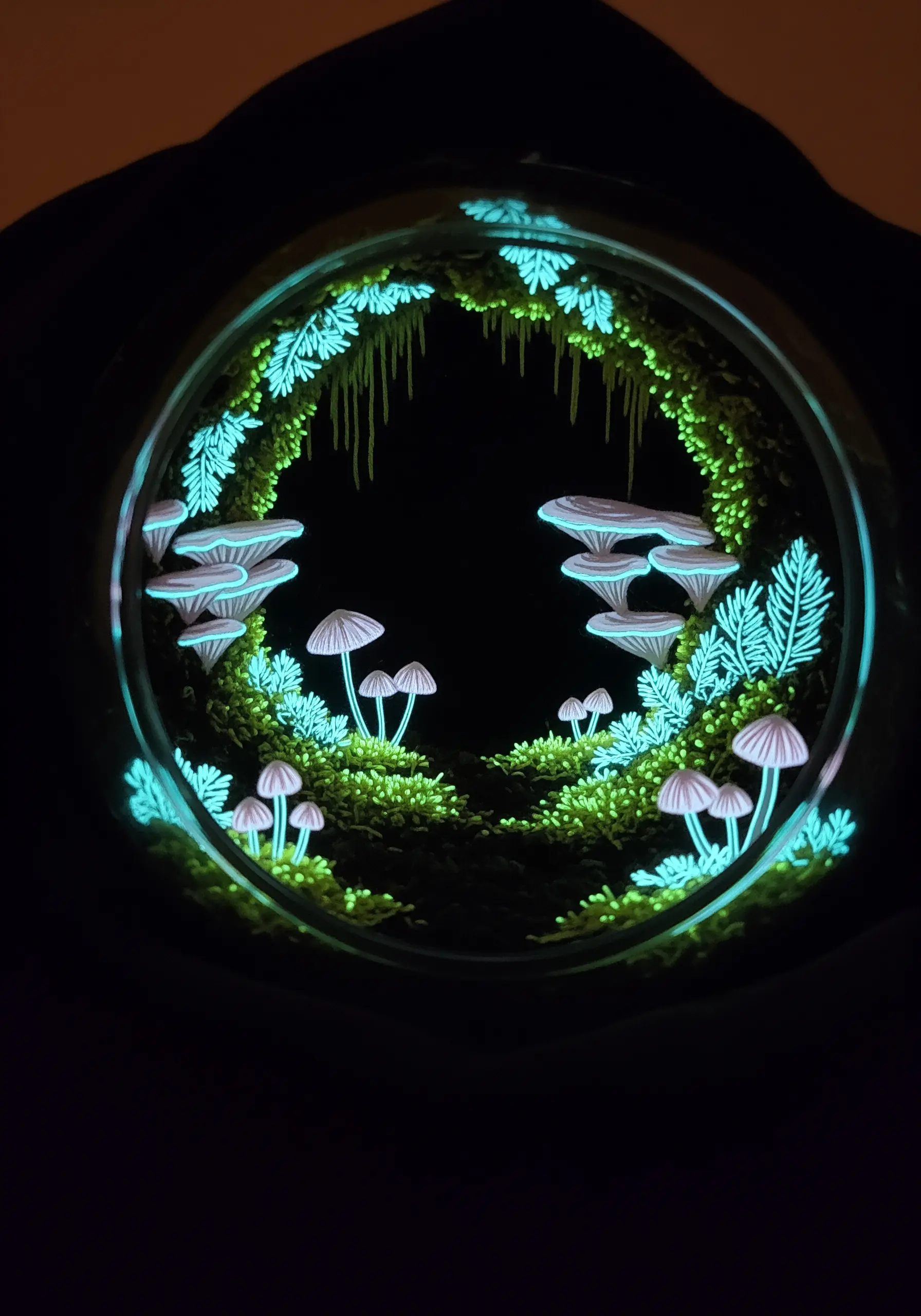 A round, portal-like embroidery of a glowing mushroom grotto on black fabric
