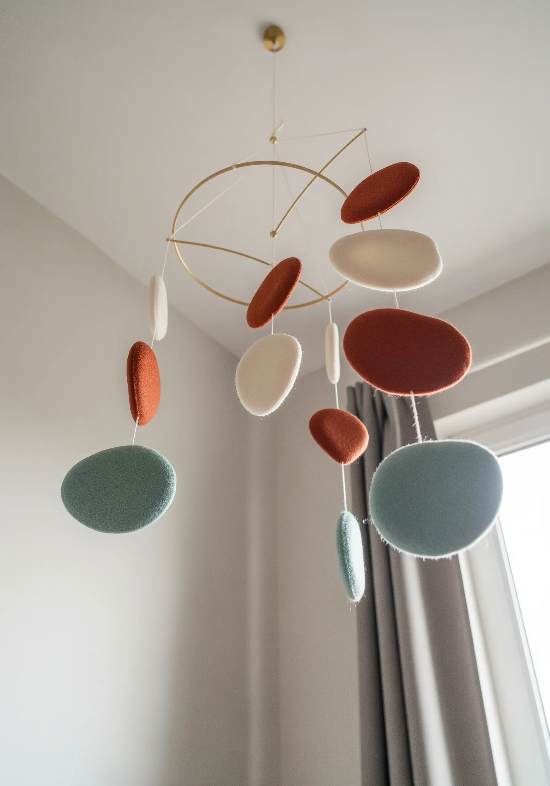A modern, minimalist mobile with abstract felt shapes in terracotta, cream, and dusty blue.