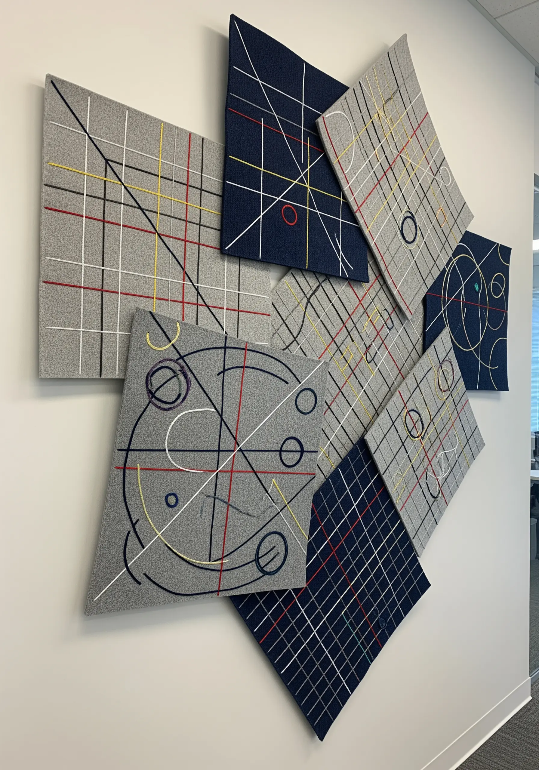 A modular wall installation of multiple embroidered panels with abstract geometric lines.