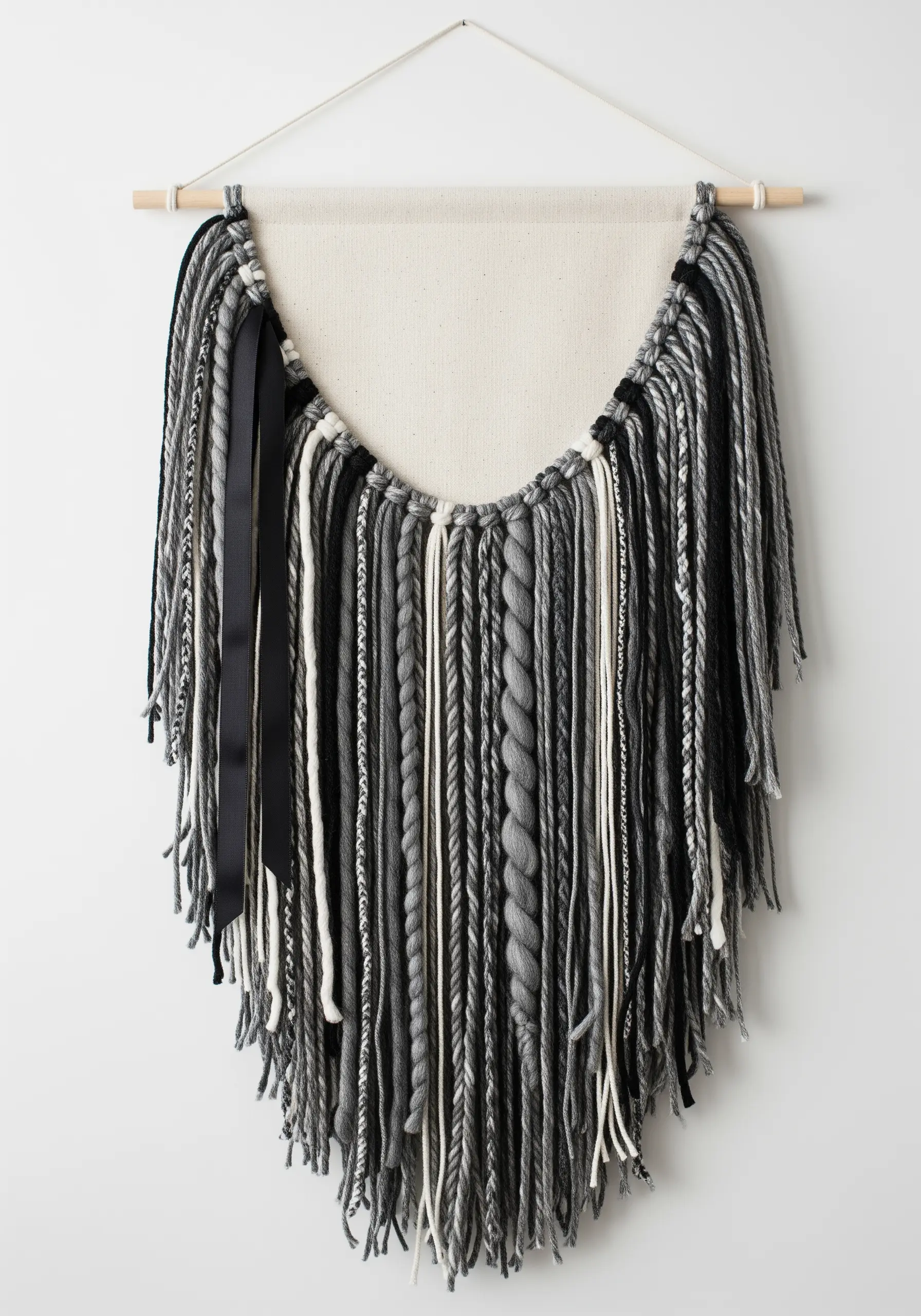 A wall hanging with cascading strands of black, grey, and white yarn in various textures.