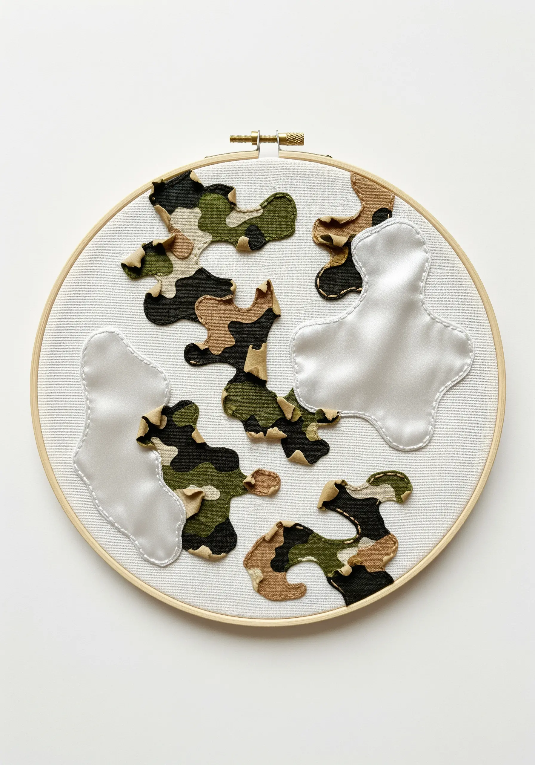 Abstract hoop art using appliqué with camouflage and white satin fabric shapes.