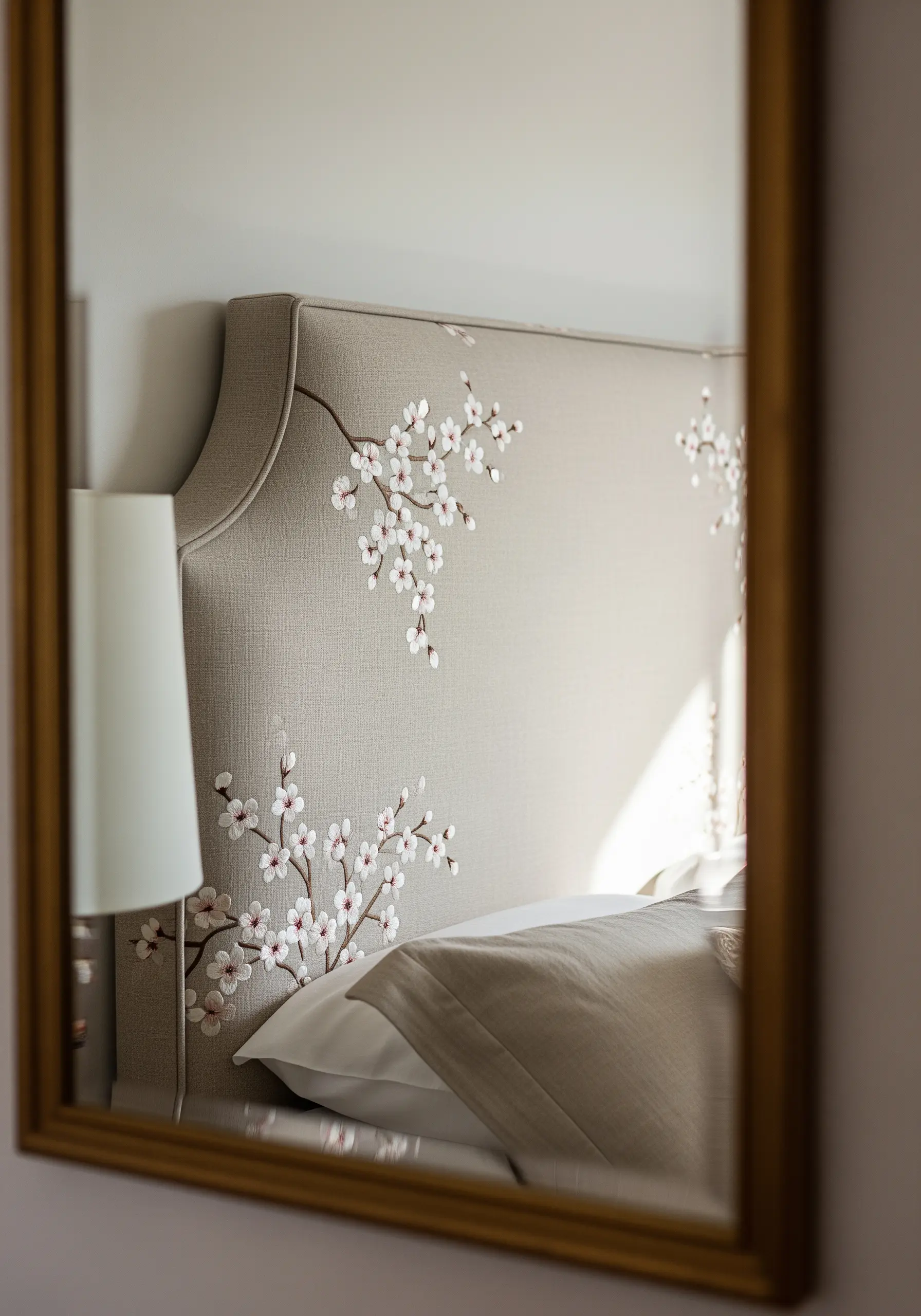 A reflection in a mirror shows a neutral upholstered headboard with embroidered cherry blossoms.