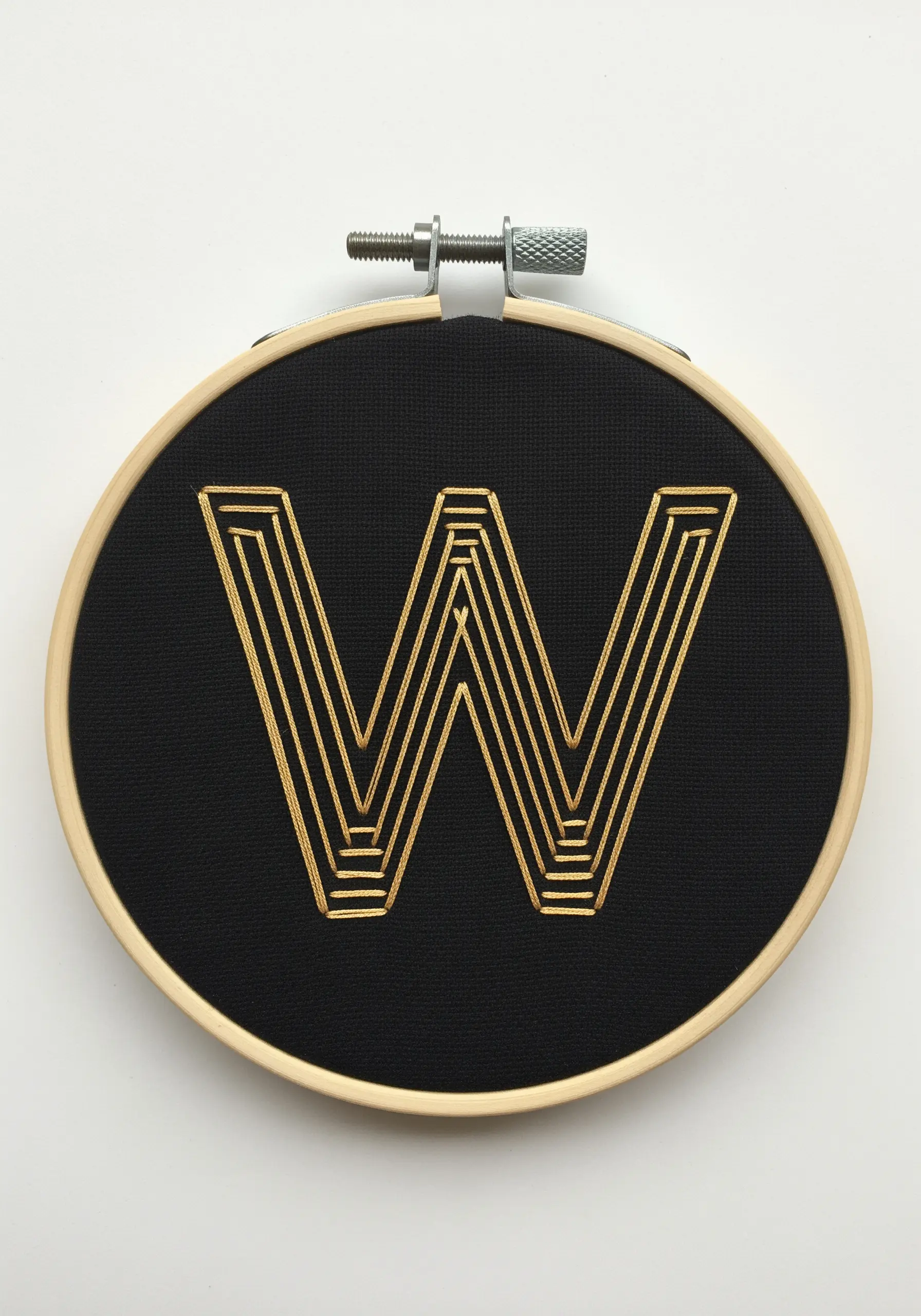A gold letter 'W' created with concentric backstitch outlines on black fabric.