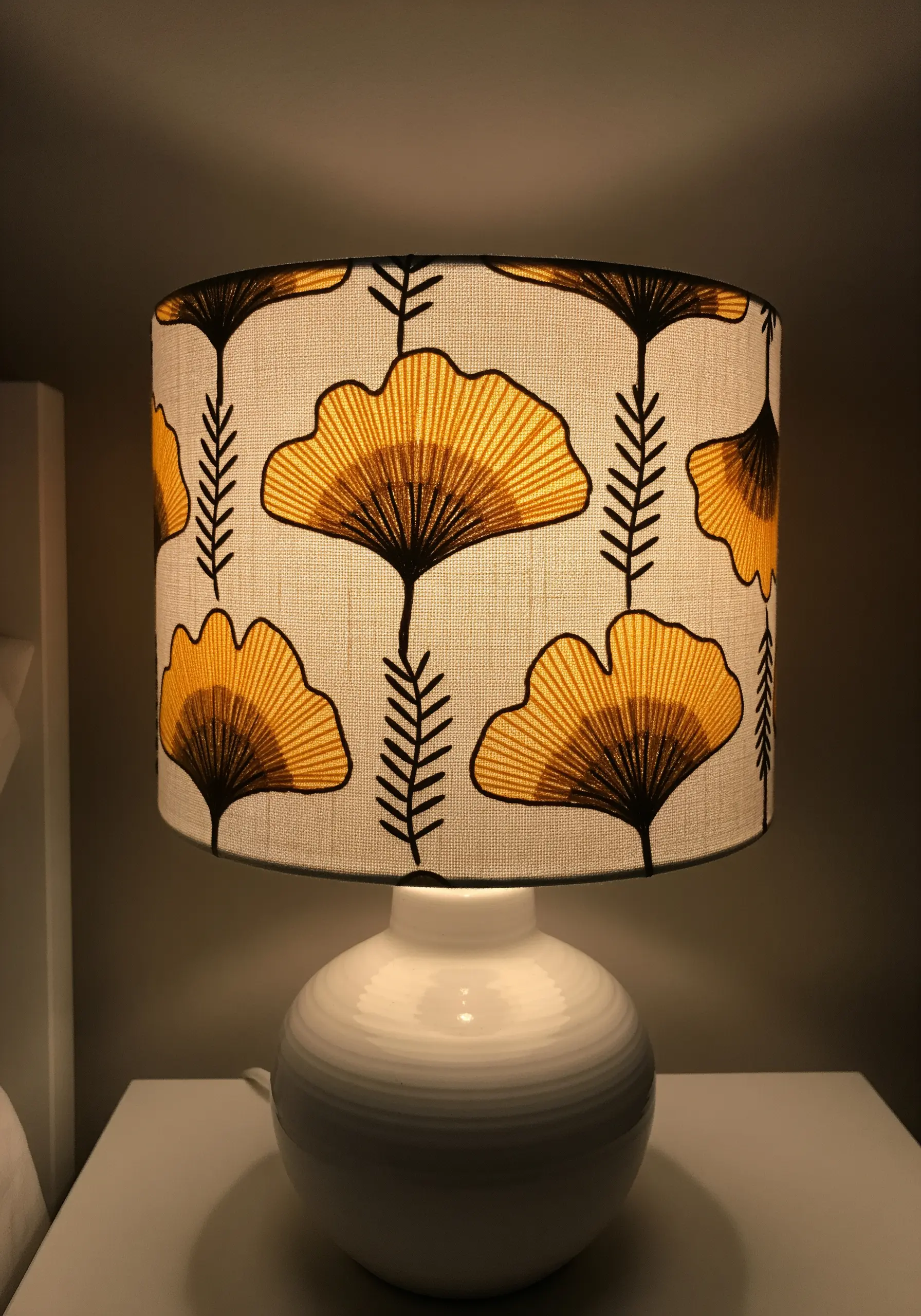 A drum lampshade with an embroidered pattern of yellow and black ginkgo leaves.