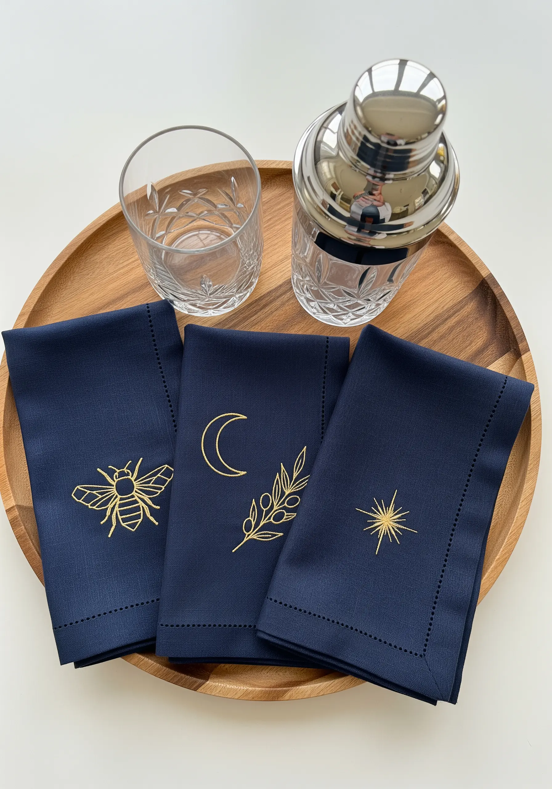 Three navy blue cocktail napkins, each with a single minimalist gold motif: a bee, a moon, a star.
