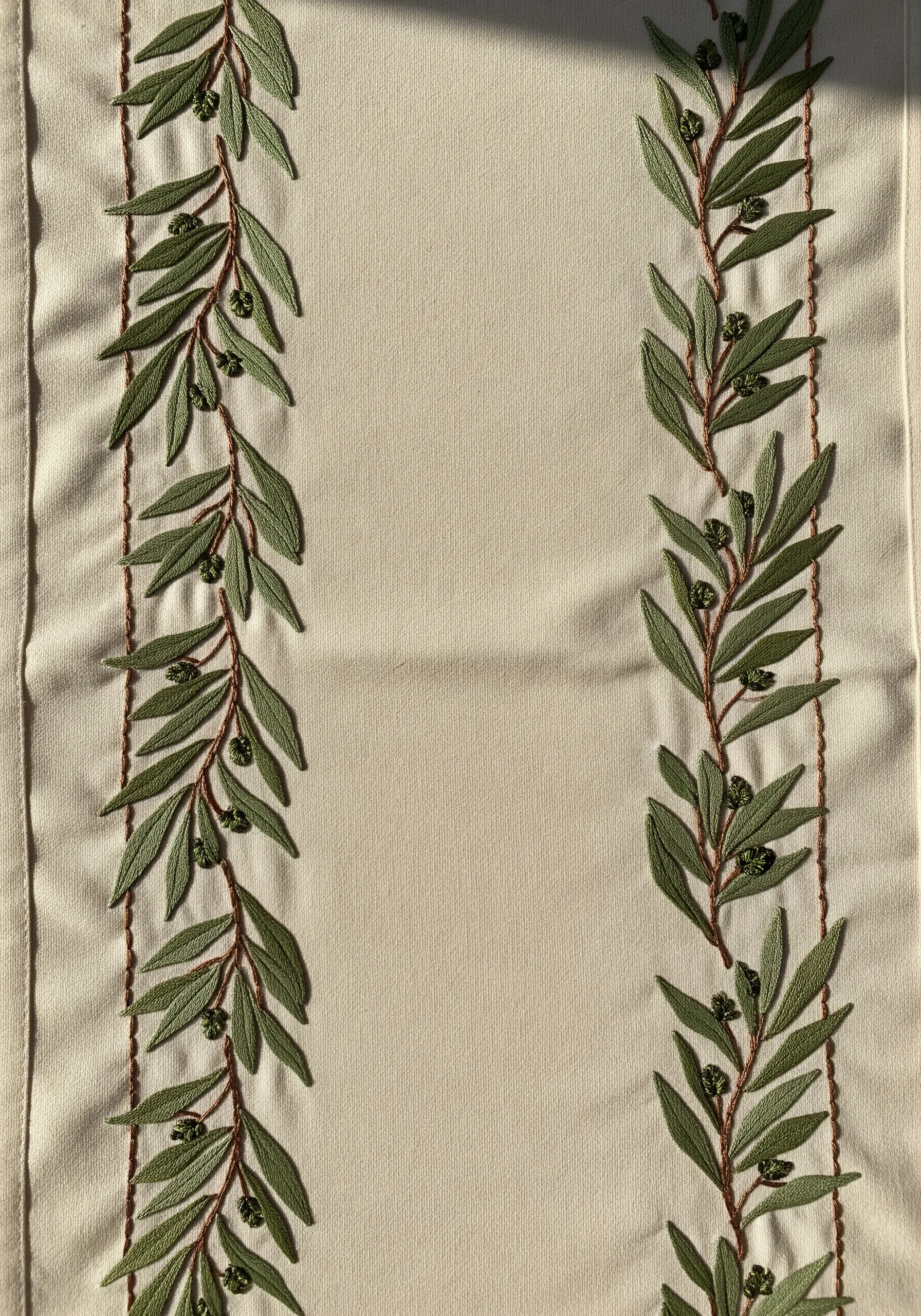 Two parallel borders of embroidered olive branches with green leaves and small black olives.