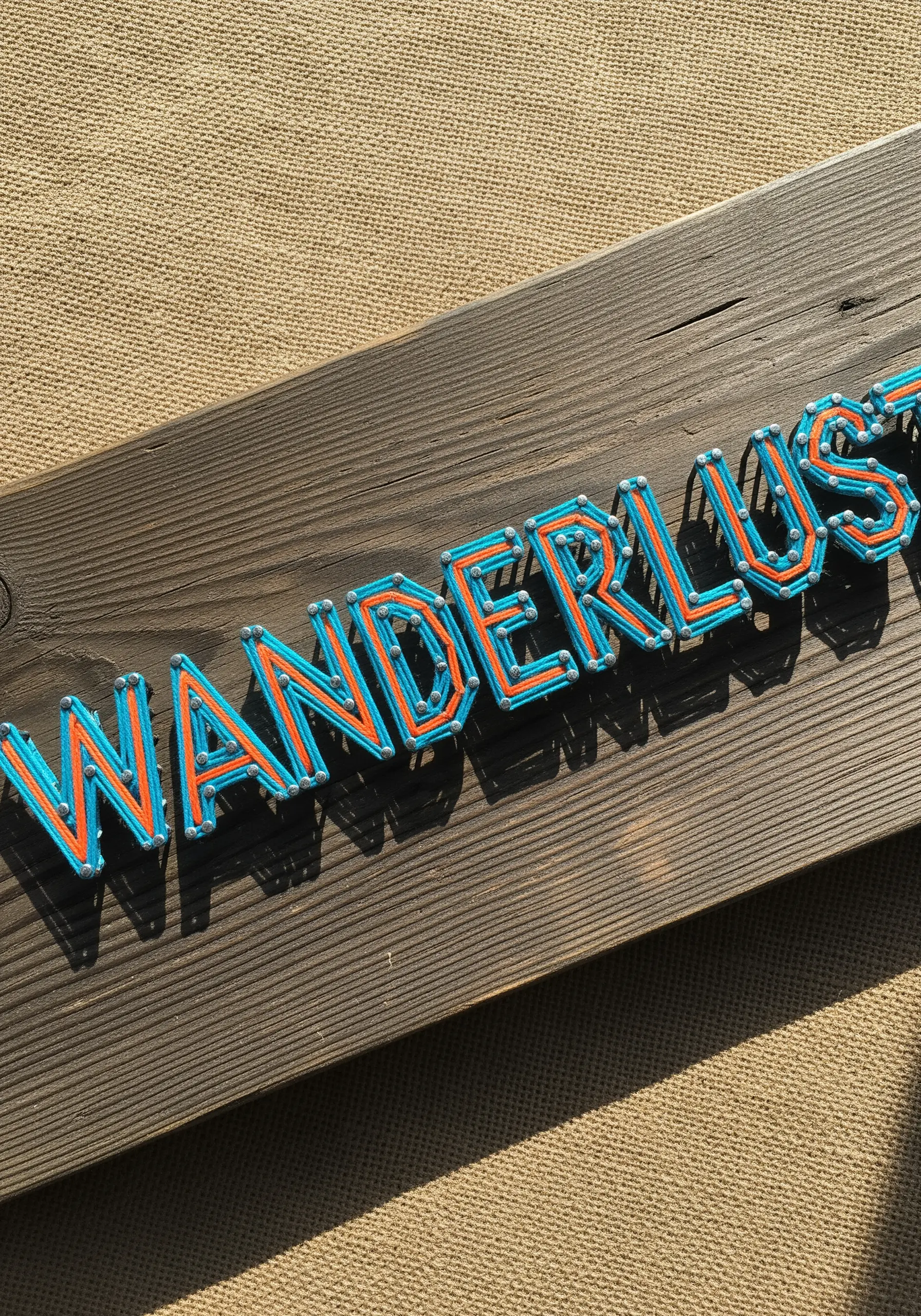 Blue and orange string art typography on dark wood showing tight nail spacing