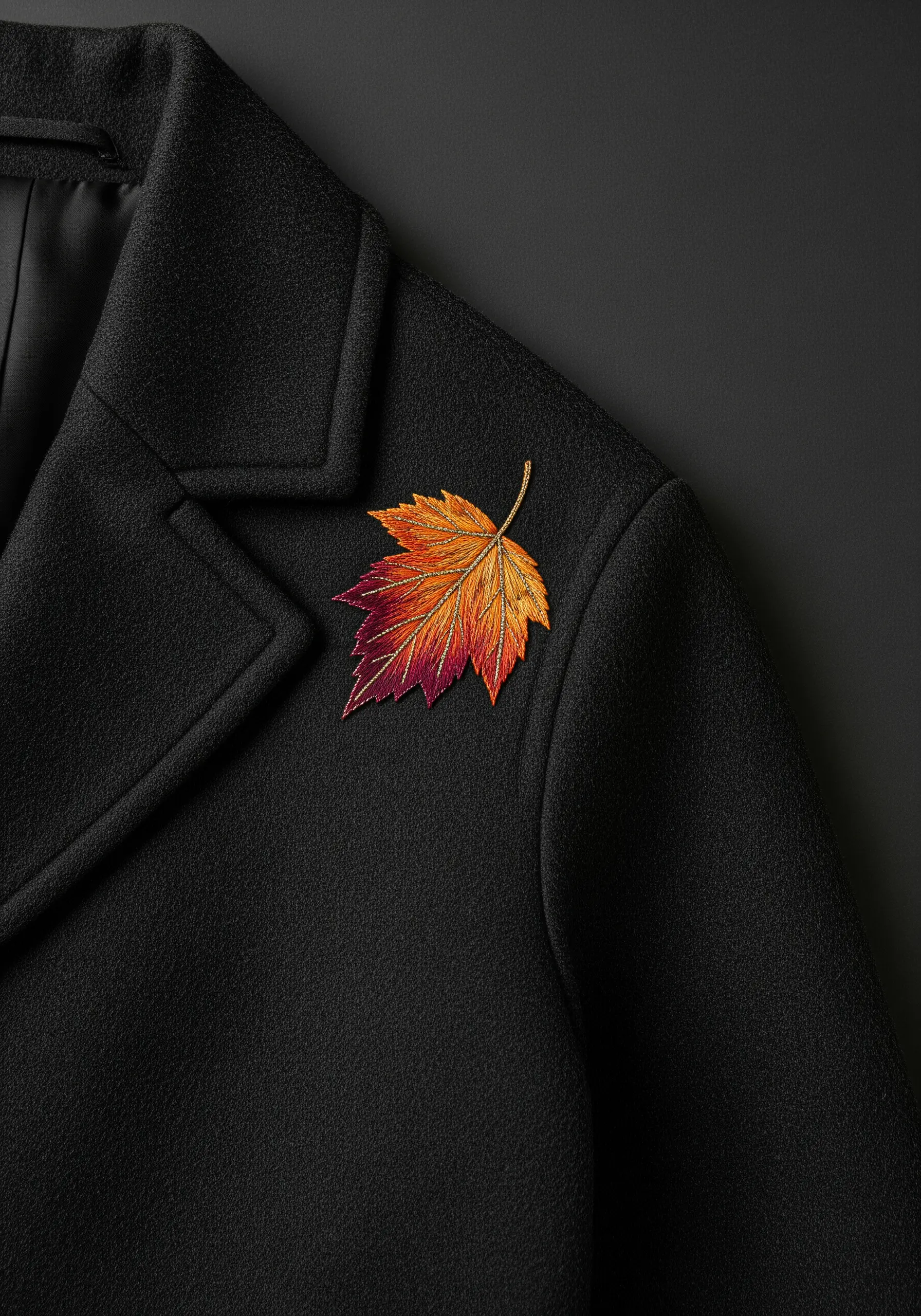Embroidered 3D autumn leaf with gradient colors on a black coat lapel.
