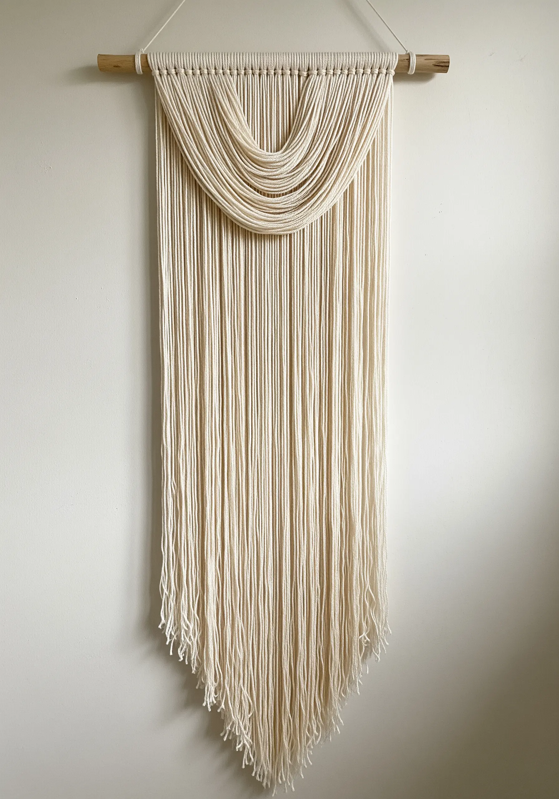 A minimalist wall hanging made of draped cream-colored yarn hanging from a wooden dowel.