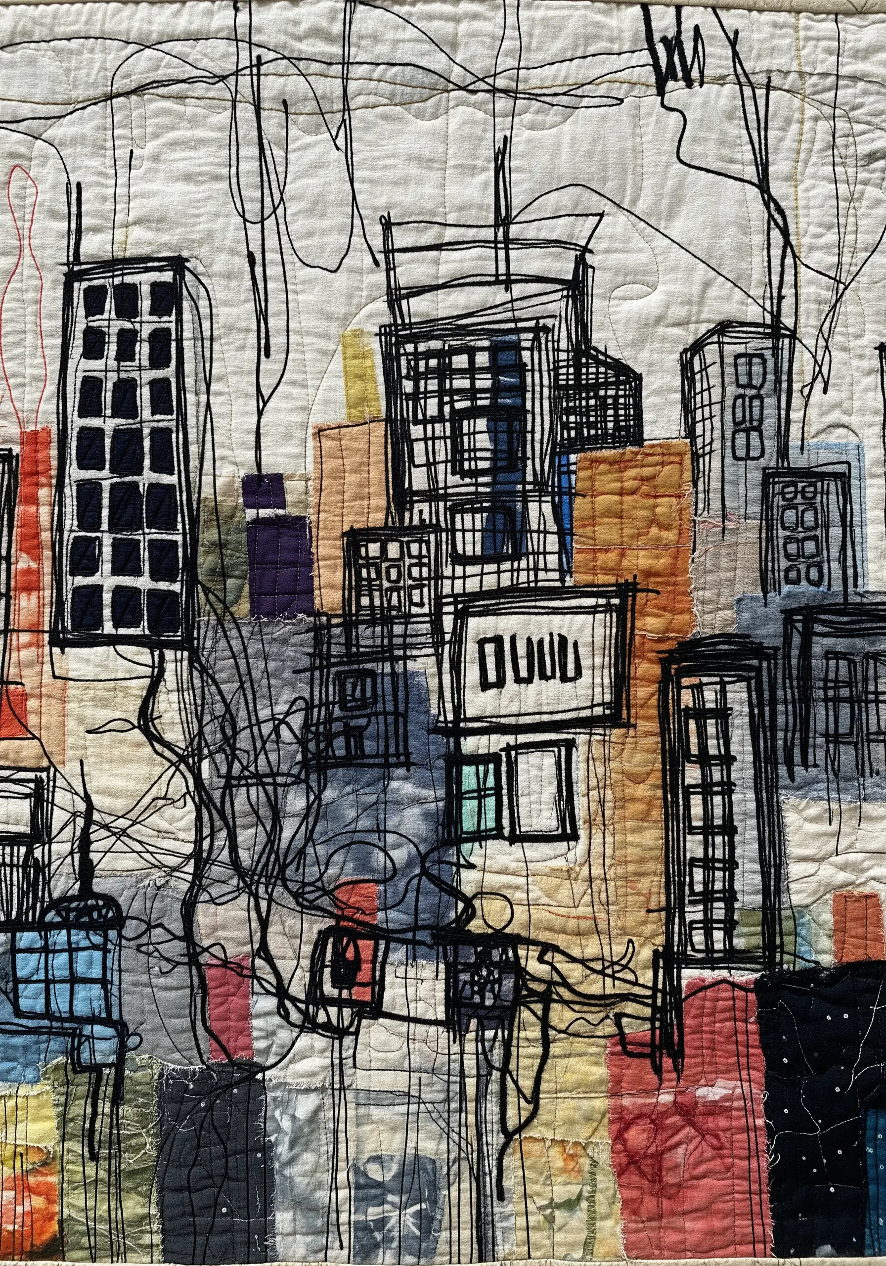 A textile art quilt of a cityscape, created with fabric collage and expressive black free-motion stitching.