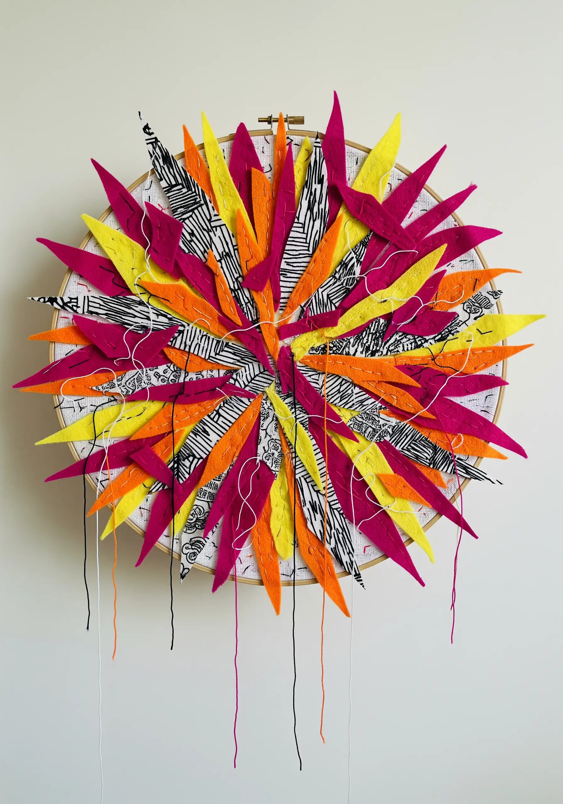 Hoop art with a radial burst of pink, yellow, orange, and patterned felt pieces.