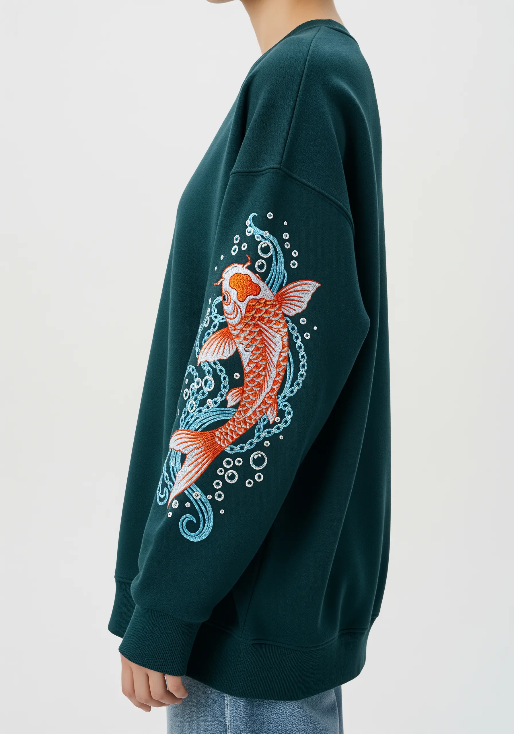 Embroidered orange and white koi fish swimming amidst blue water swirls on a dark green sweatshirt sleeve.