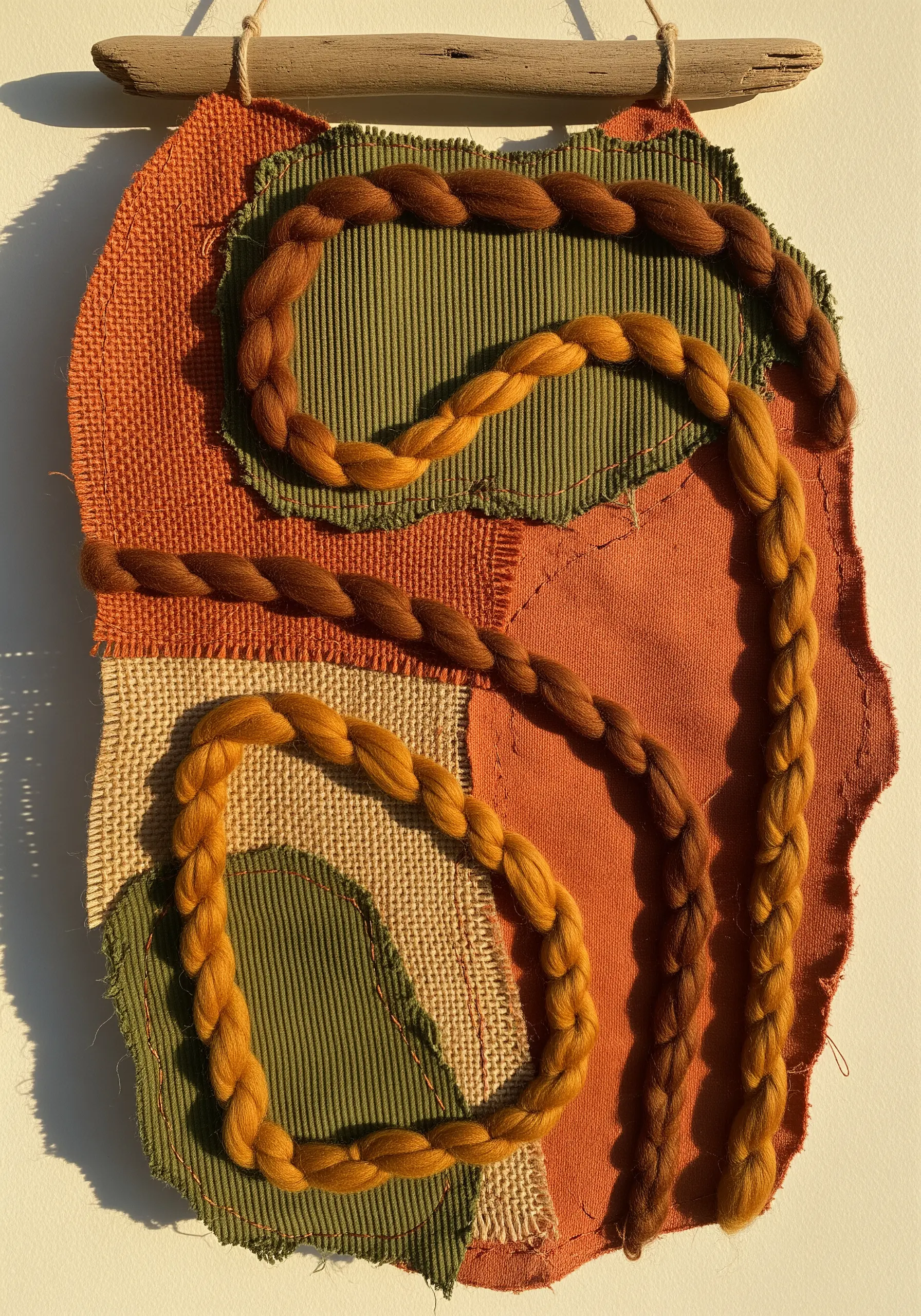 Earthy fabric collage with thick, braided wool roving stitched in curving lines.