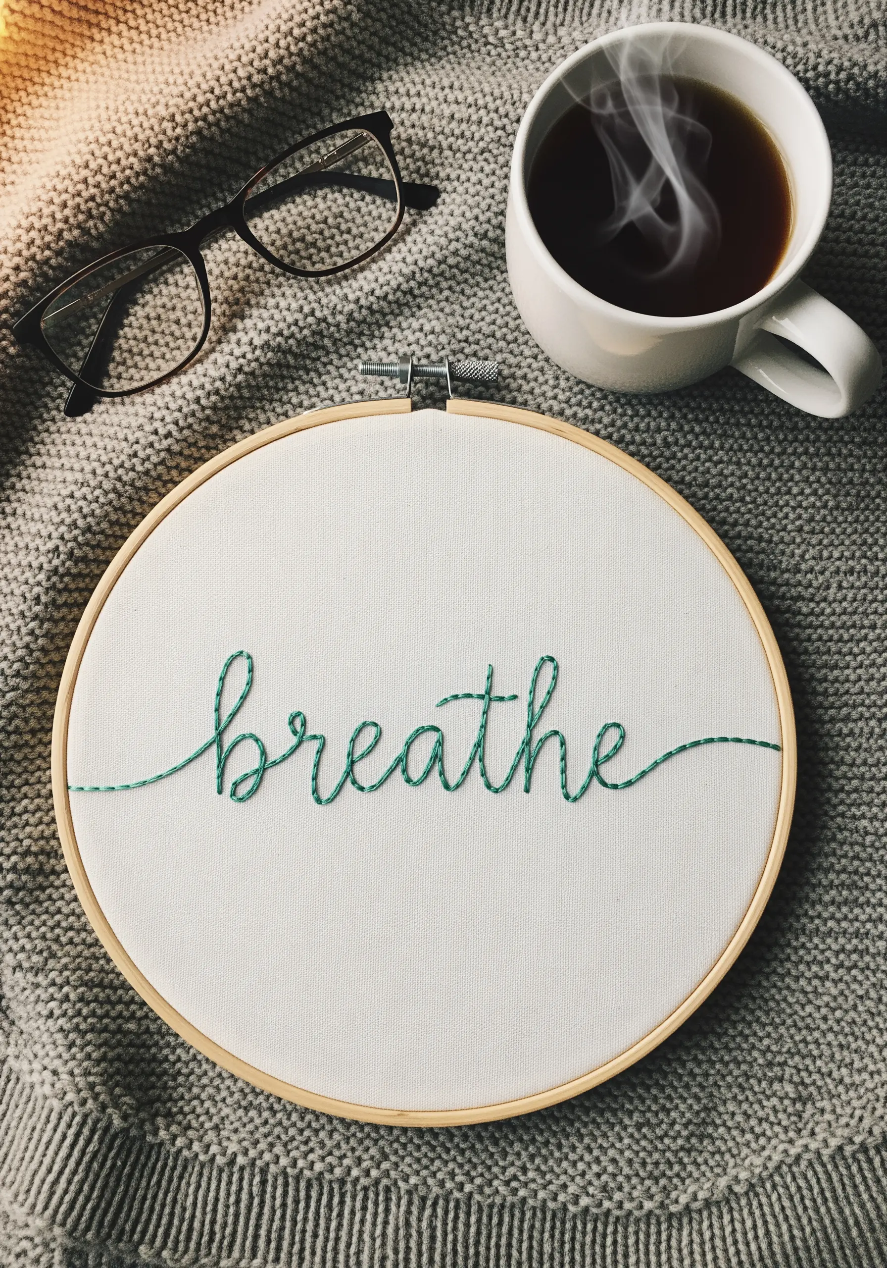The word 'breathe' stitched in green cursive thread on white fabric in a hoop.
