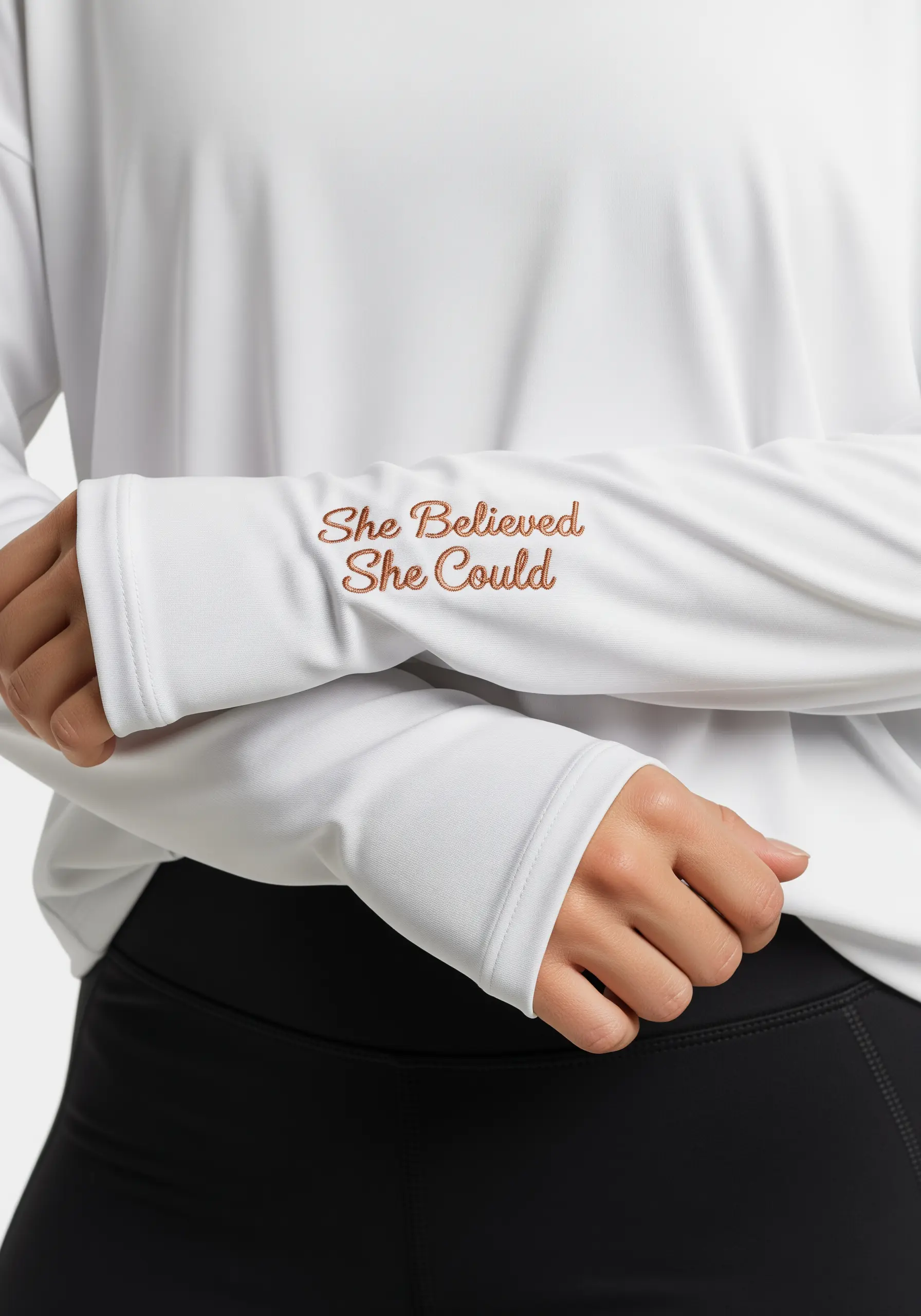 “She Believed She Could” in metallic copper script on the cuff of a white long-sleeved shirt.
