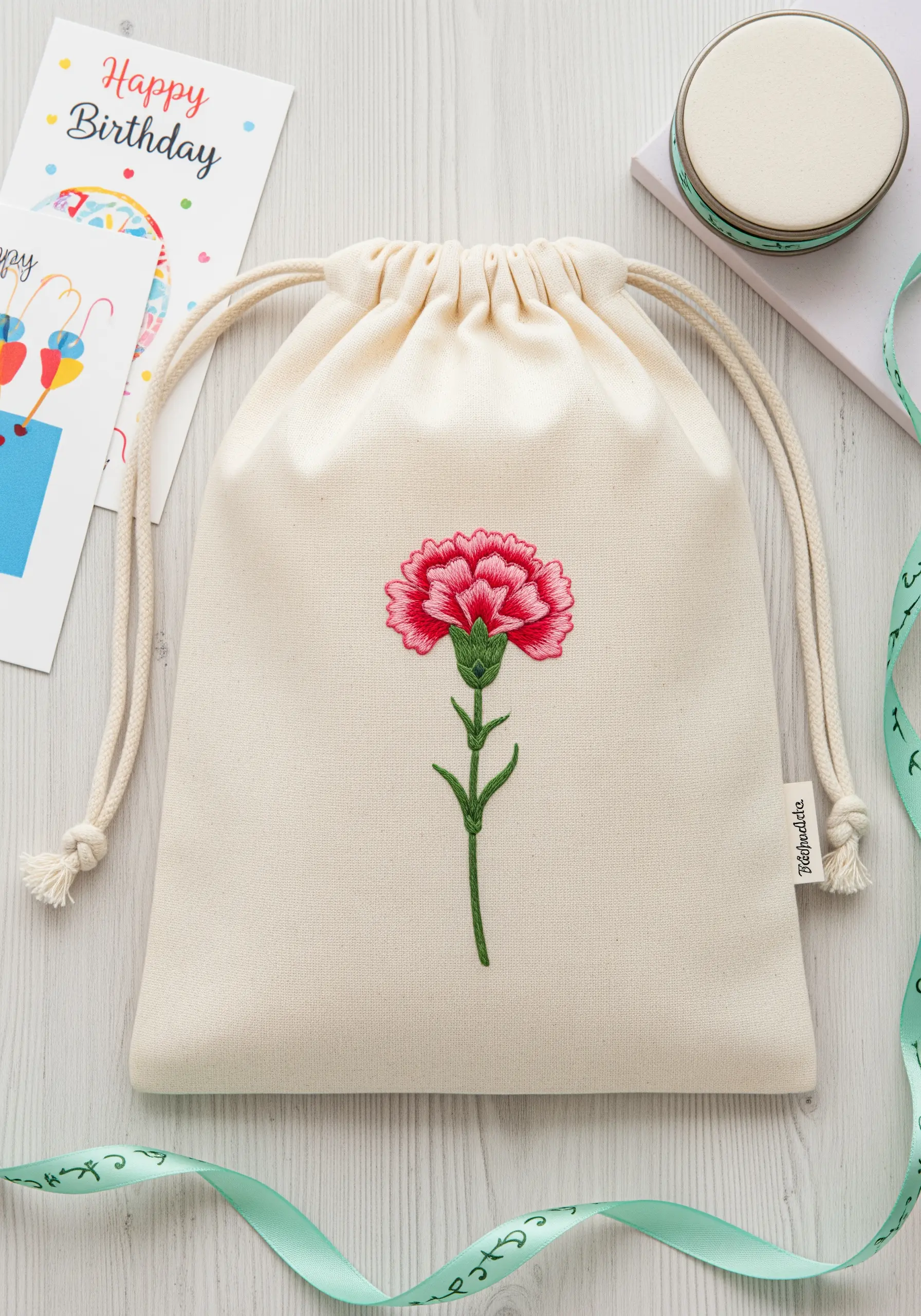 A canvas drawstring bag embroidered with a single, realistic pink and red carnation.