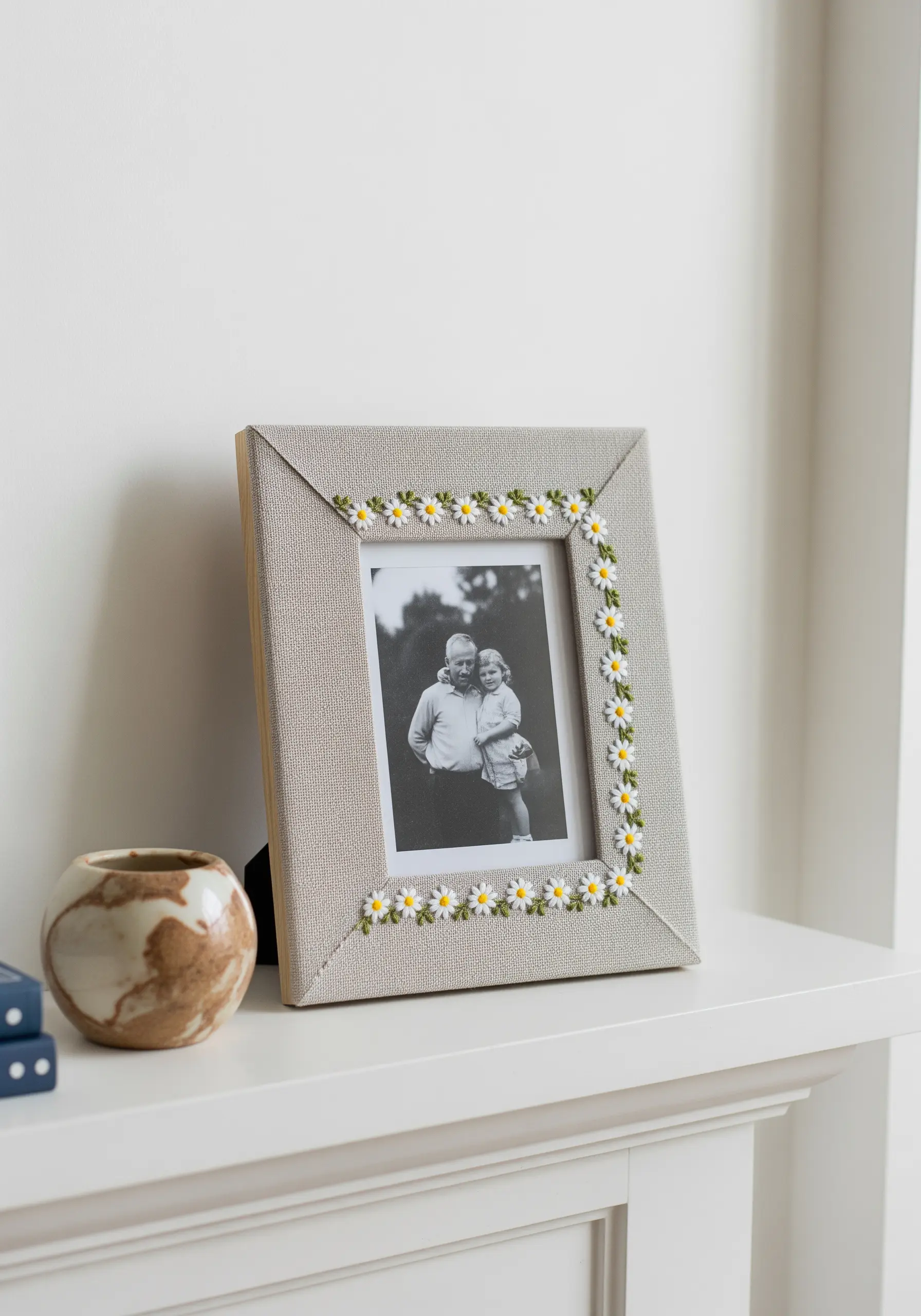 A fabric-covered photo frame embellished with a border of small, embroidered daisies.